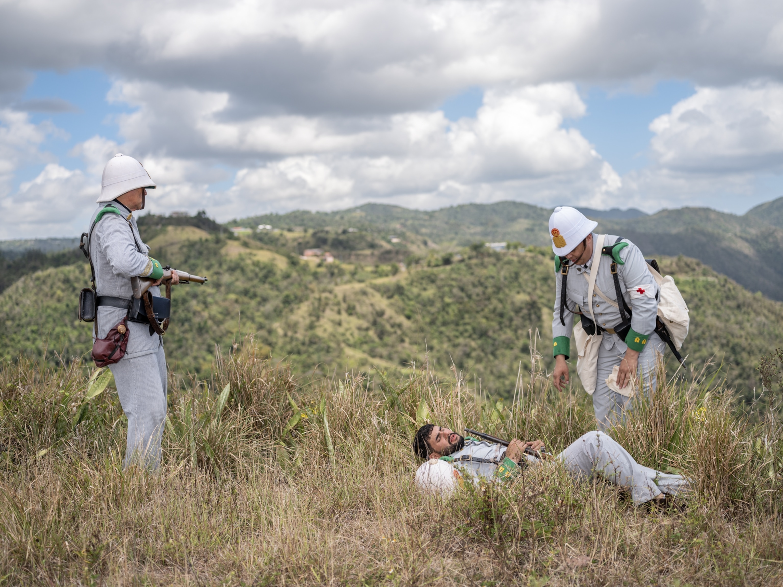 One soldier with weapon and one military soldier helping another one pretending to be wounded.