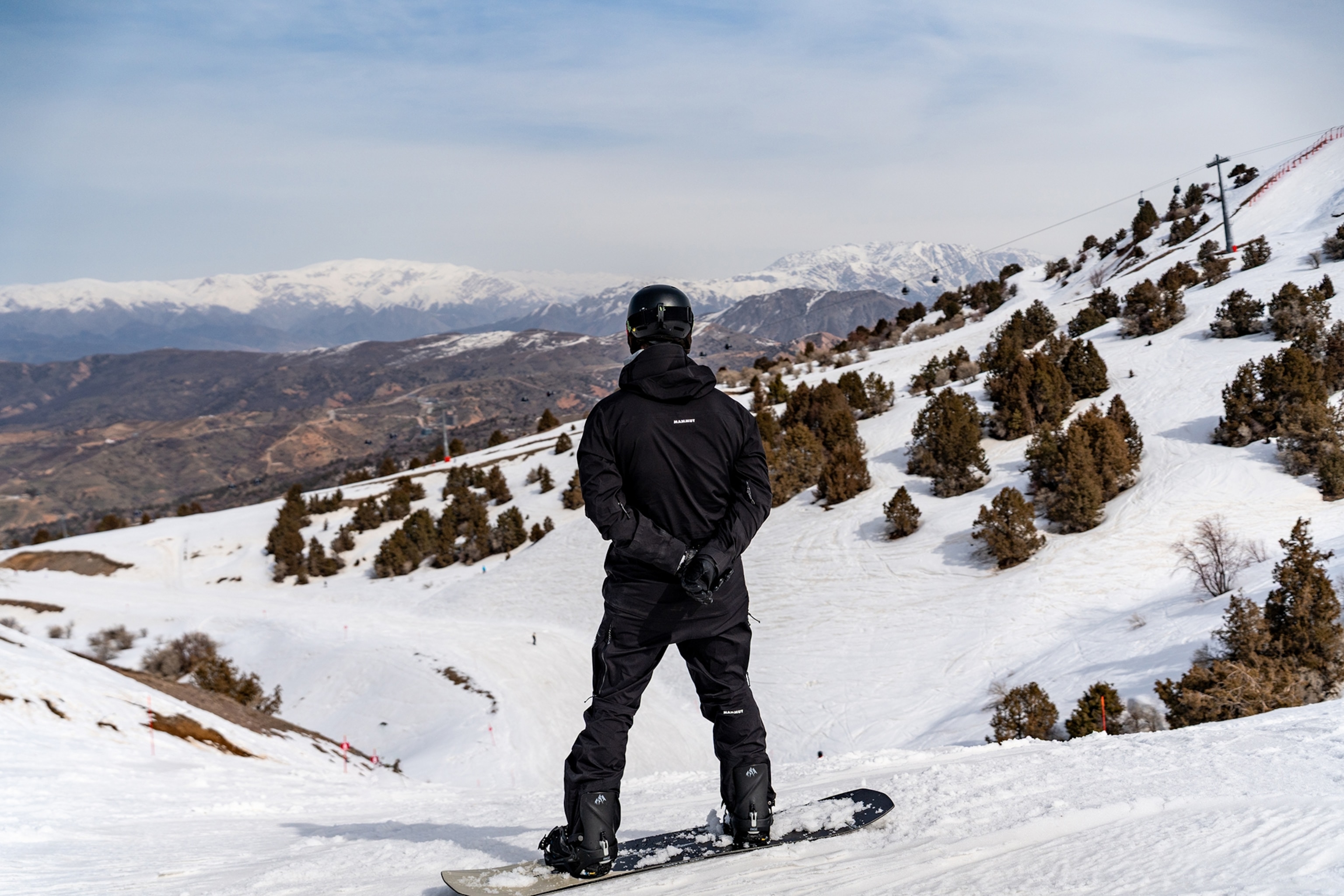 A male snowboarder looking out across a mountain landscape.