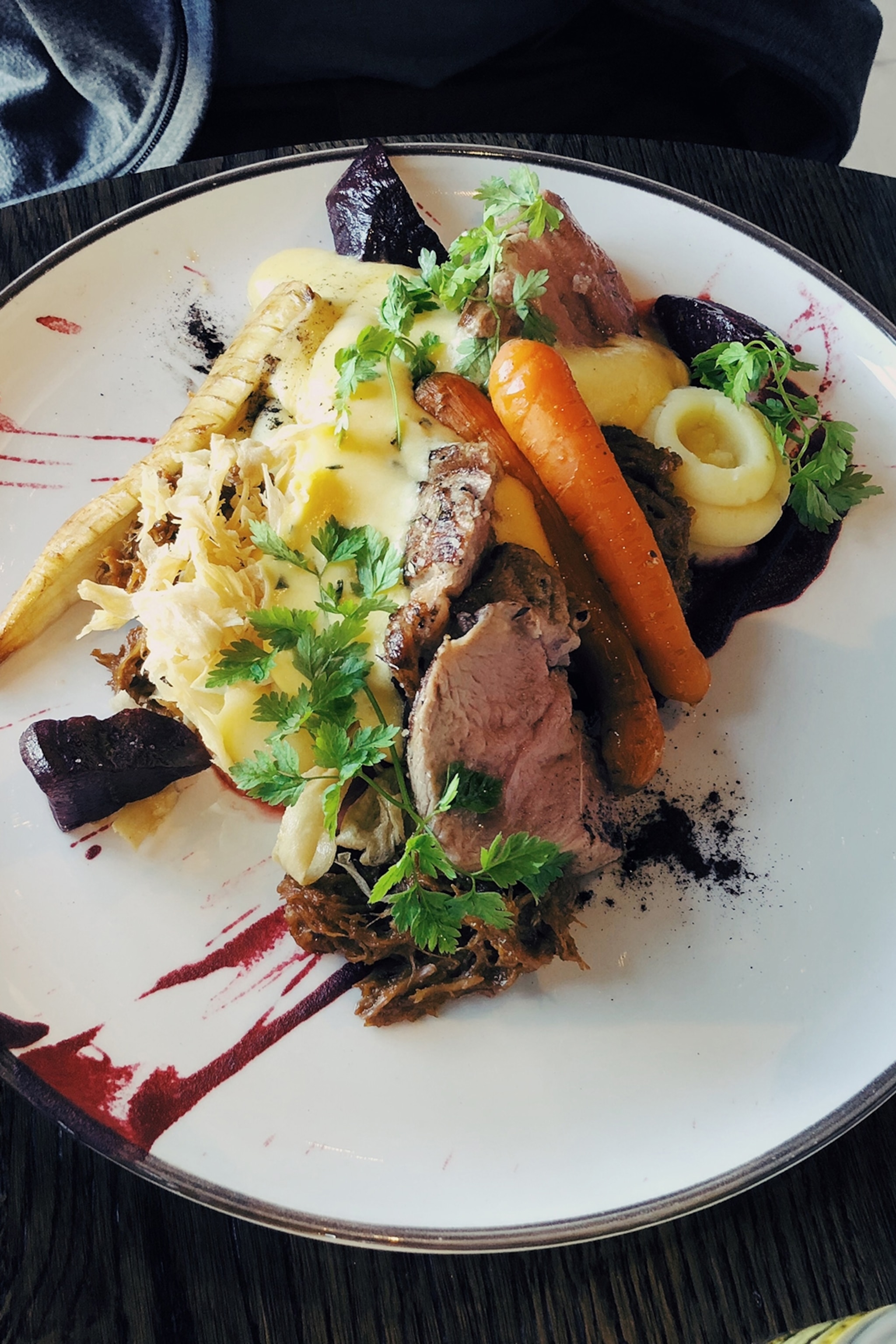 Knife and fork cutting into a pink piece of meat and vegetables served on a plate
