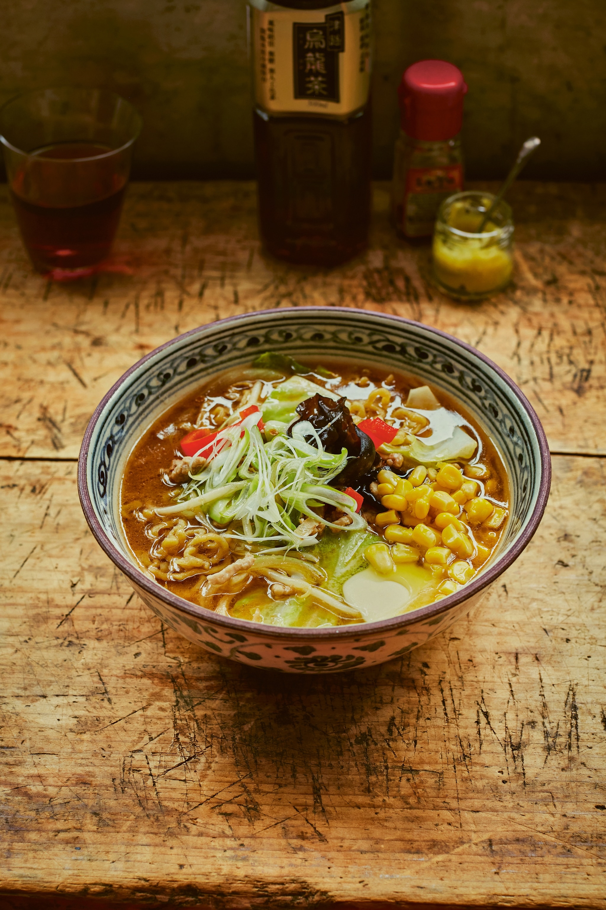 A bowl of ramen in broth, topped with sweetcorn, spring onions, kelp and pickled daikon