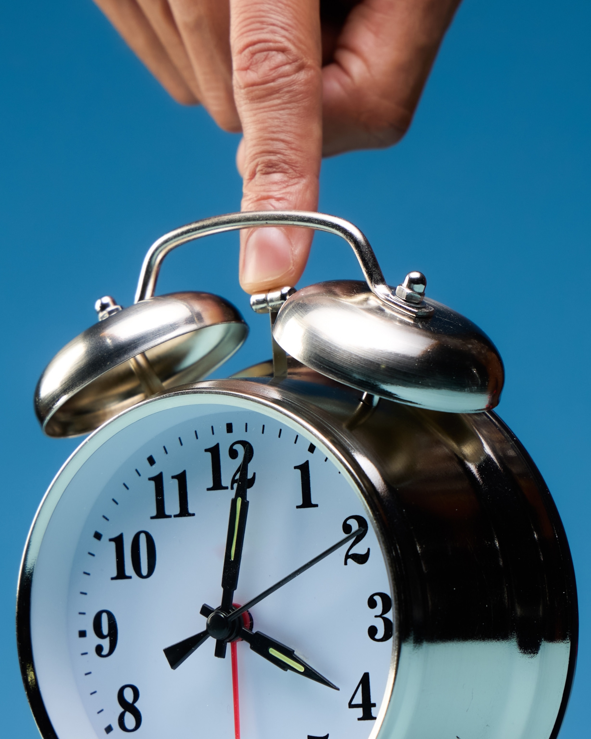 A finger pushes down on an alarm clock on a blue background.
