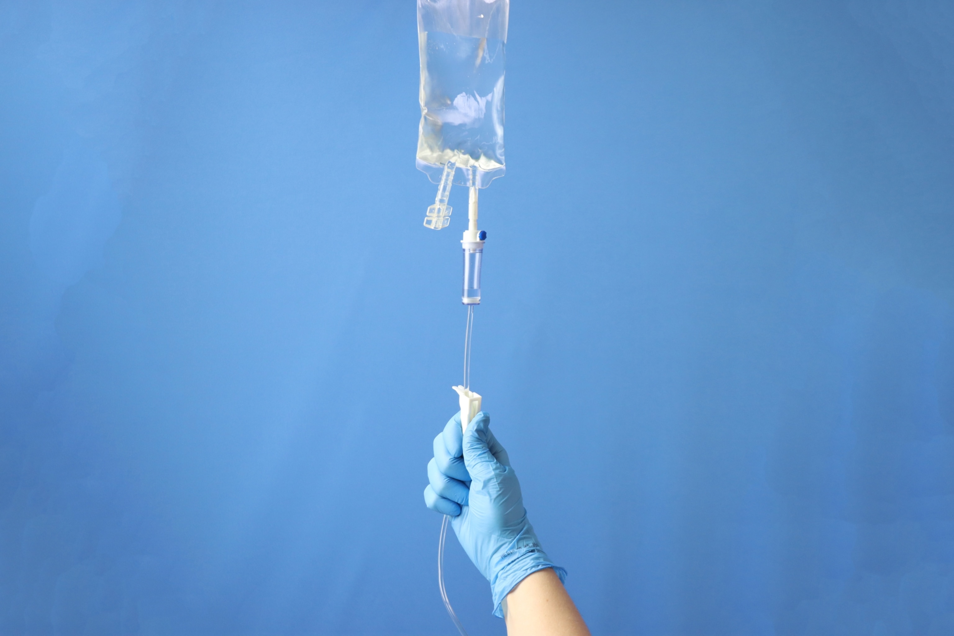 A latex-gloved hand adjusting a roller-clamp to set the drip rate of an IV