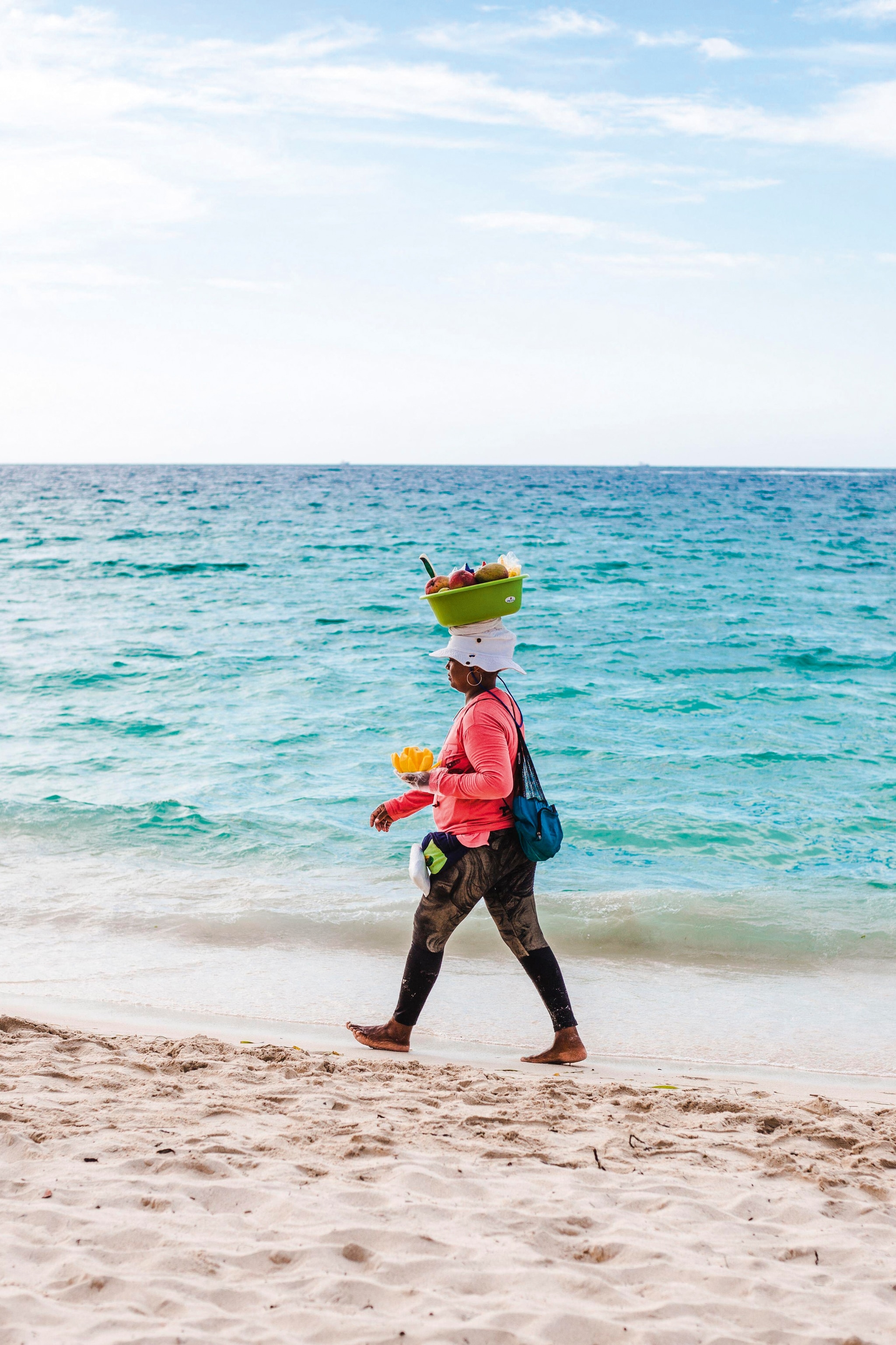 Woman walks by the sea with a basket on her head