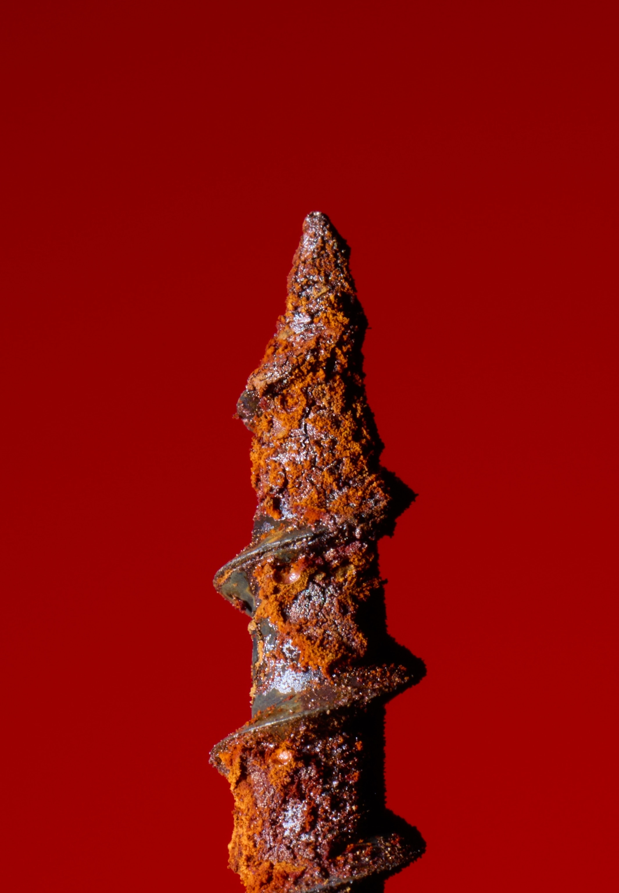A rusty screw points upward against a vibrant red background