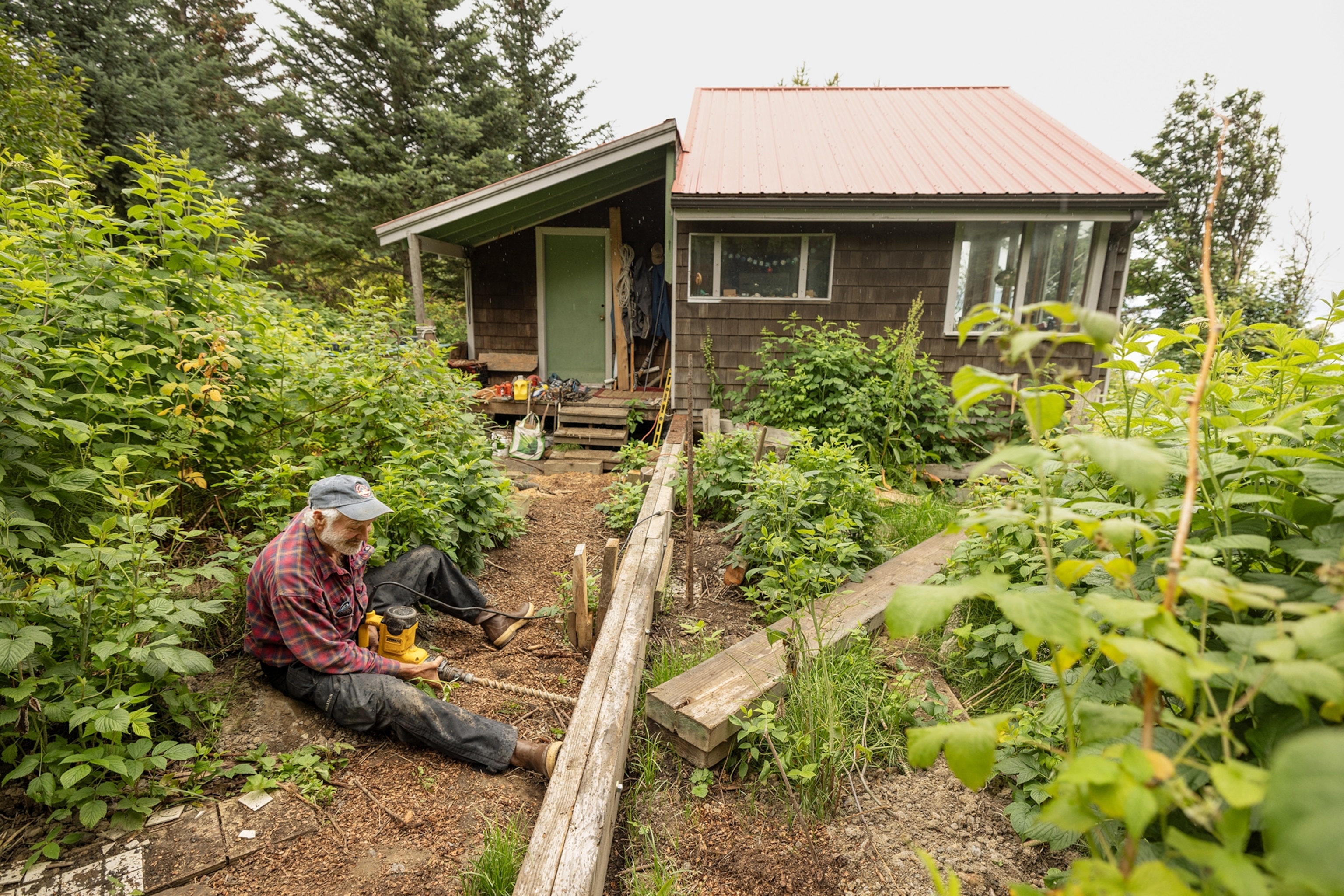 A man sits on the ground while drilling into a piece of wood.