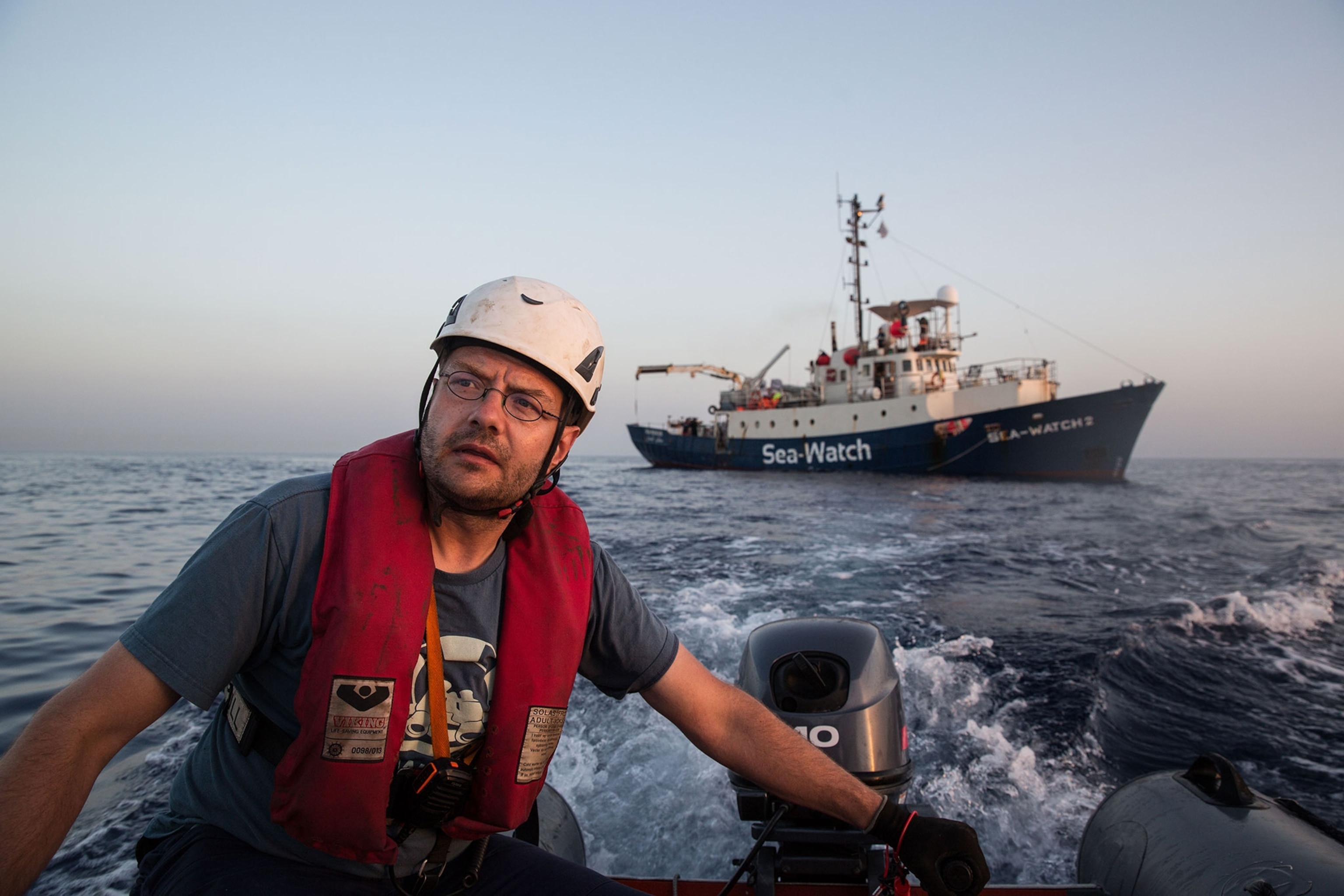 a Sea-Watch volunteer motoring a small boat away from a larger vessel