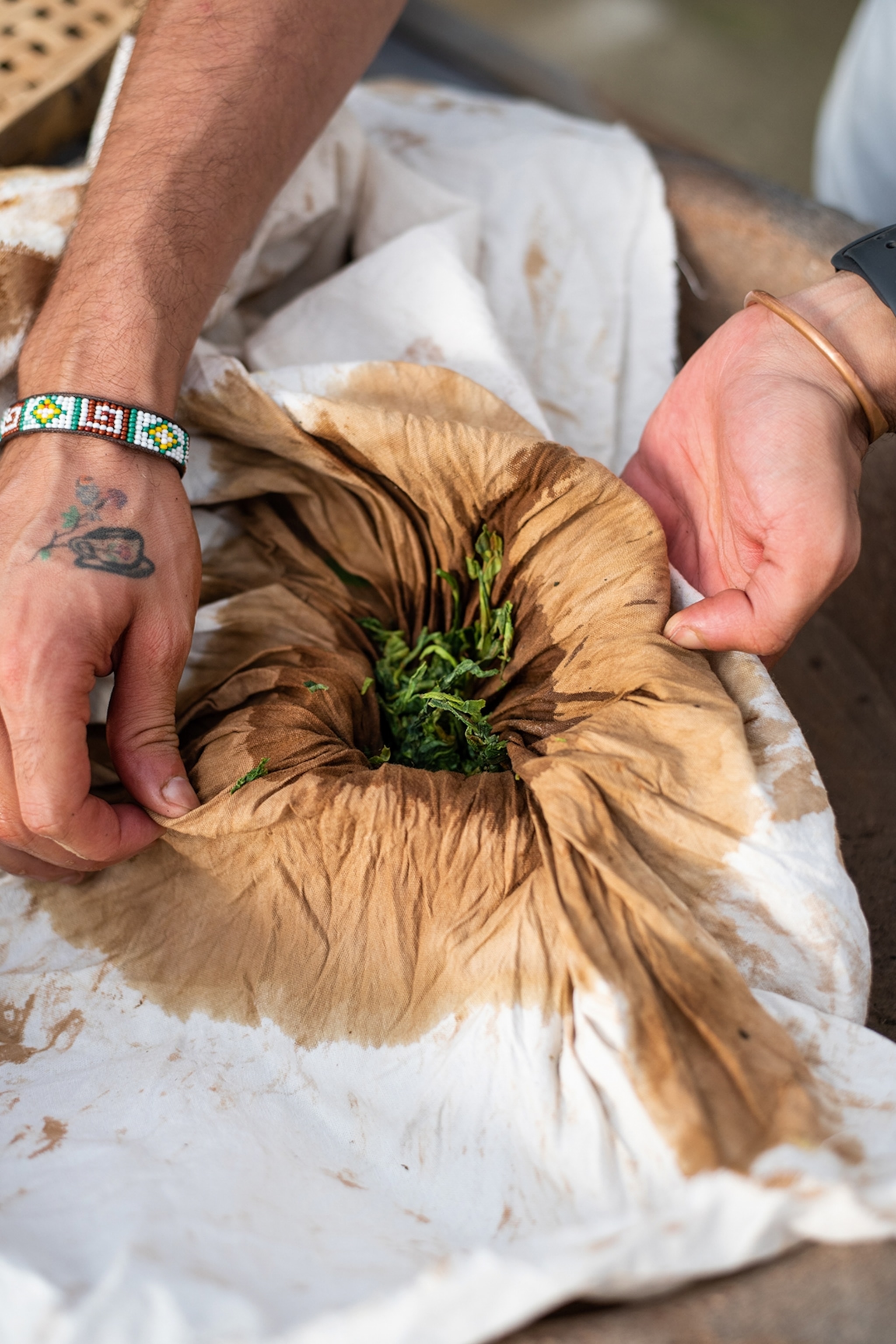 A muslin cloth with pressed tea leaves in the middle, held a pair of hands, as the stain spreads outwards.