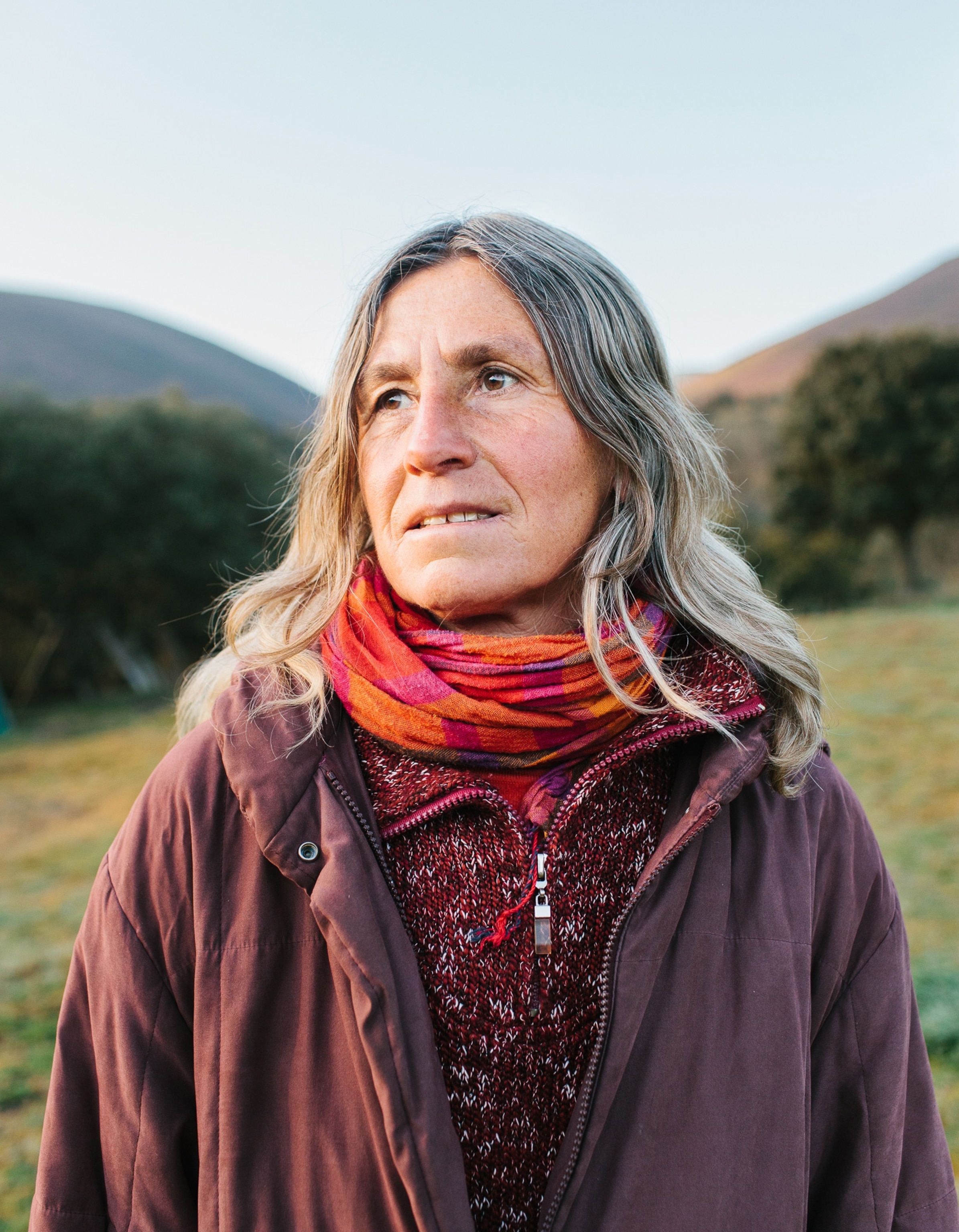 a woman dressed in purple and red, with silvery-blonde hair looking out into the distance
