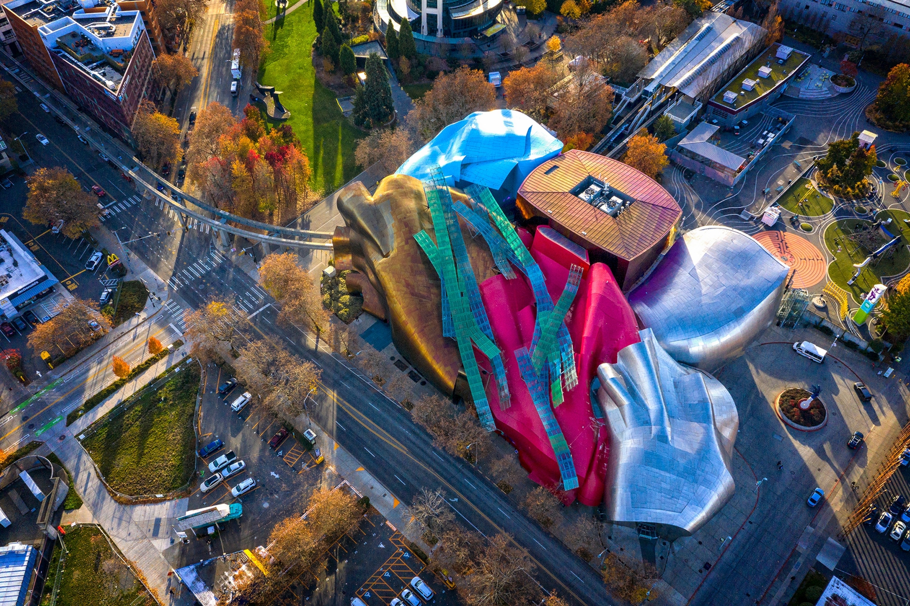 An aerial view over a compact museum with rippling a metallic roof ad sculptural details on the facade.