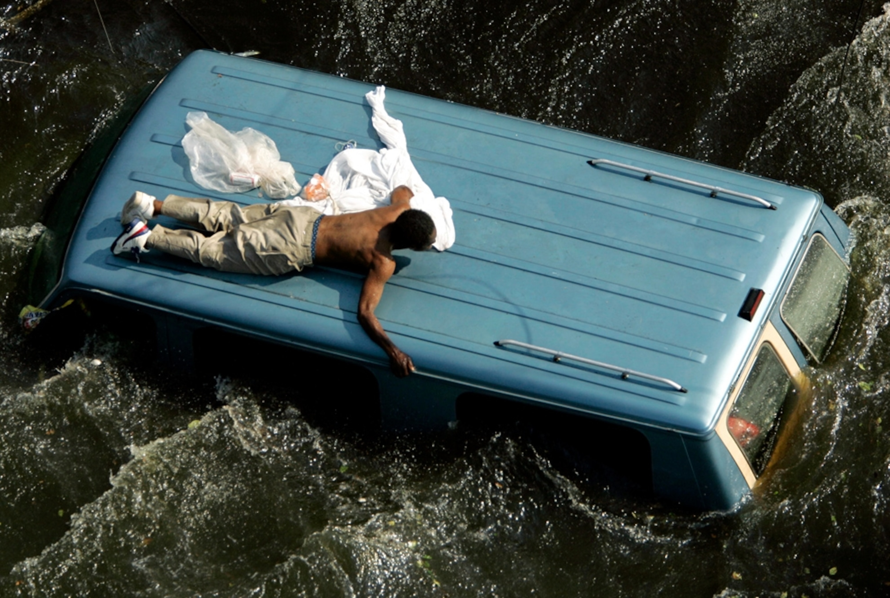 A man clings to the top of a vehicle after Hurricane Katrina.