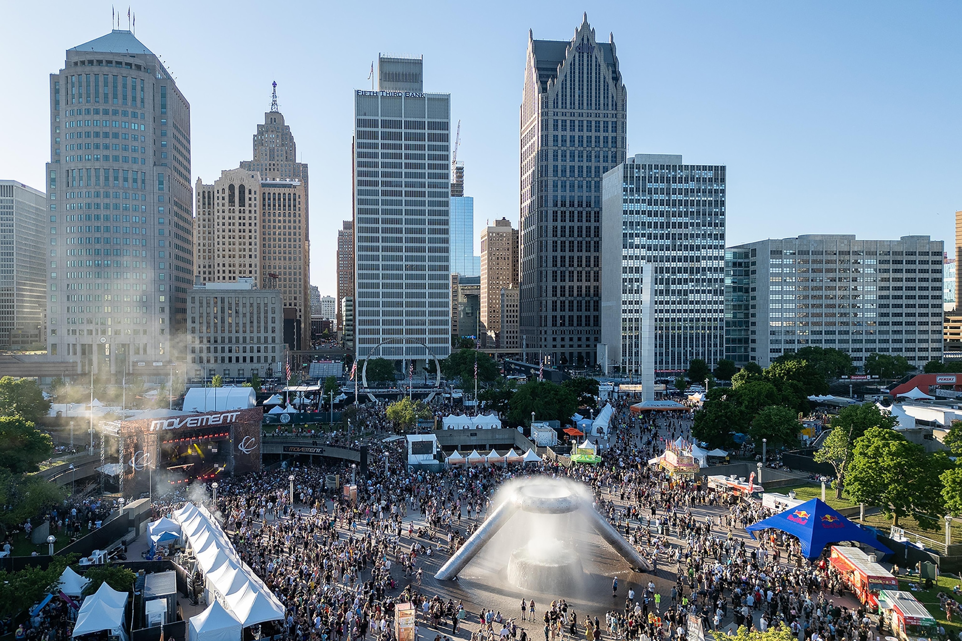 Elevated image of high-rise buildings in a city with a large outdoor space below which is filled with stages, tents and people