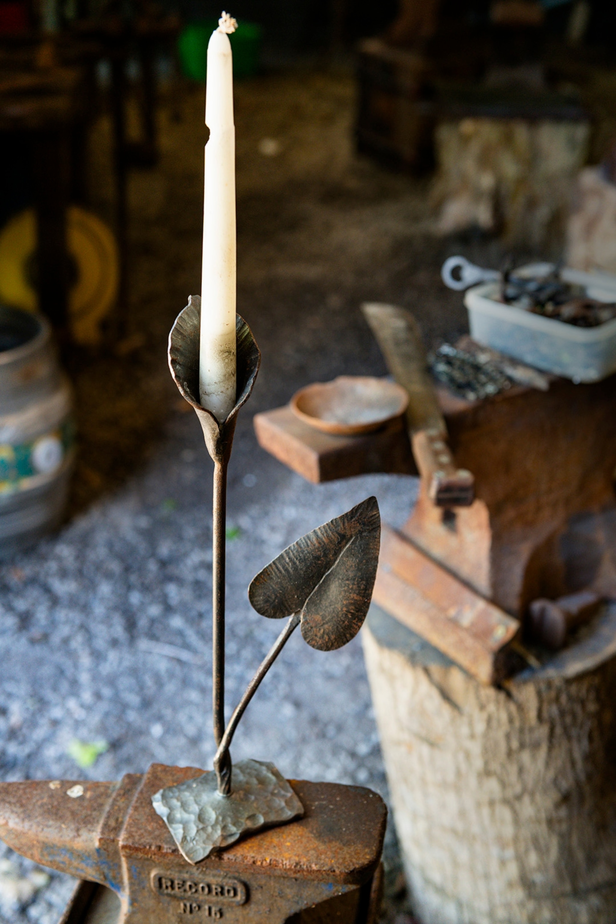 A steel candle stick in the shape of a narrow flower with a candle positioned in the centre.