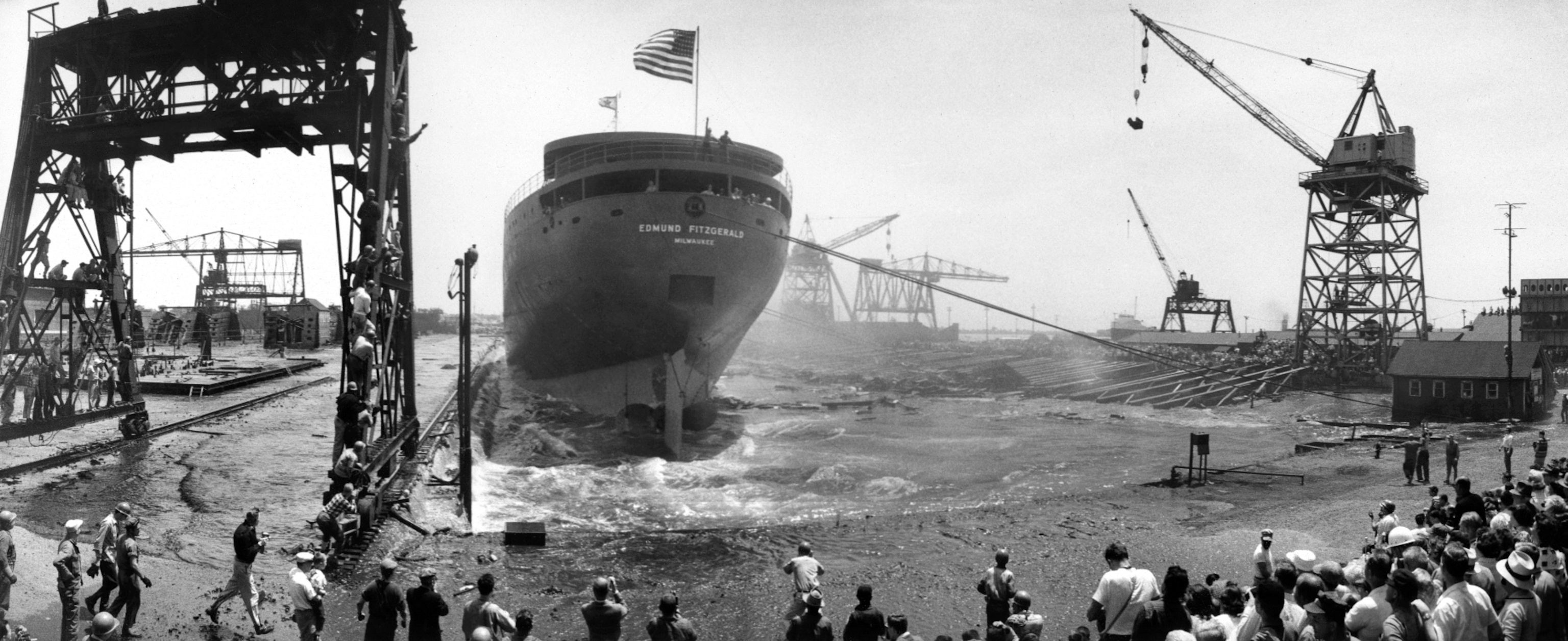 A panoramic view of the Edmund Fitzgerald rolling off the dry dock into the water before a large crowd of onlookers.