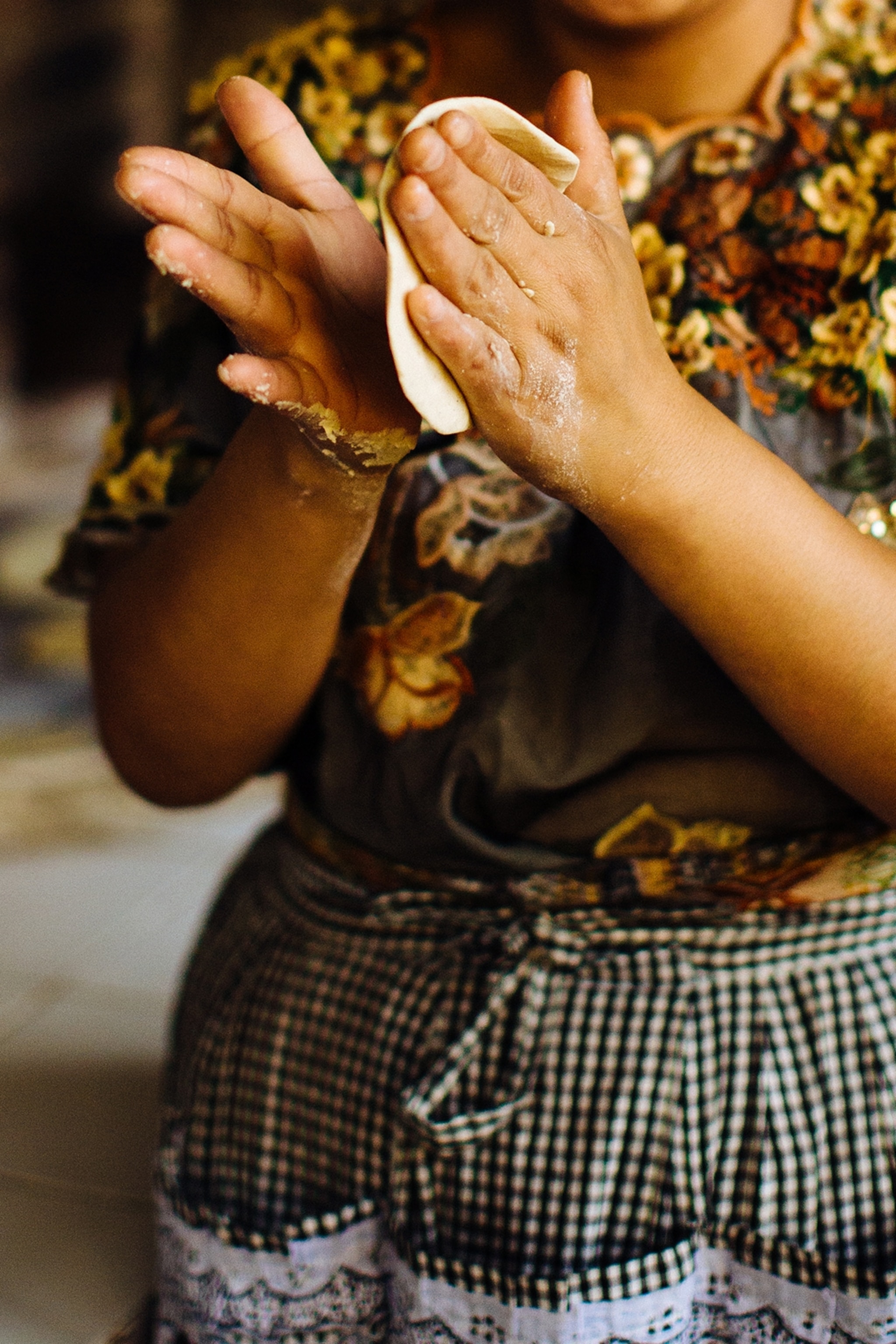 A woman shaping dough into a thick tortilla.