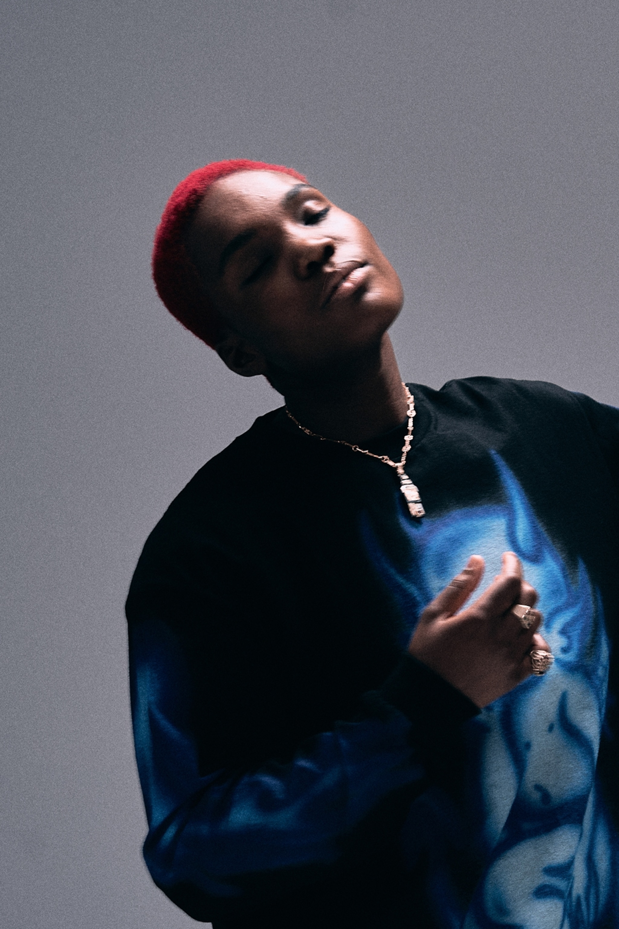 A grainy shot of a singer with a red buzz cut, wearing a graphic sweatshirt and seemingly moving to music with her eyes closed.