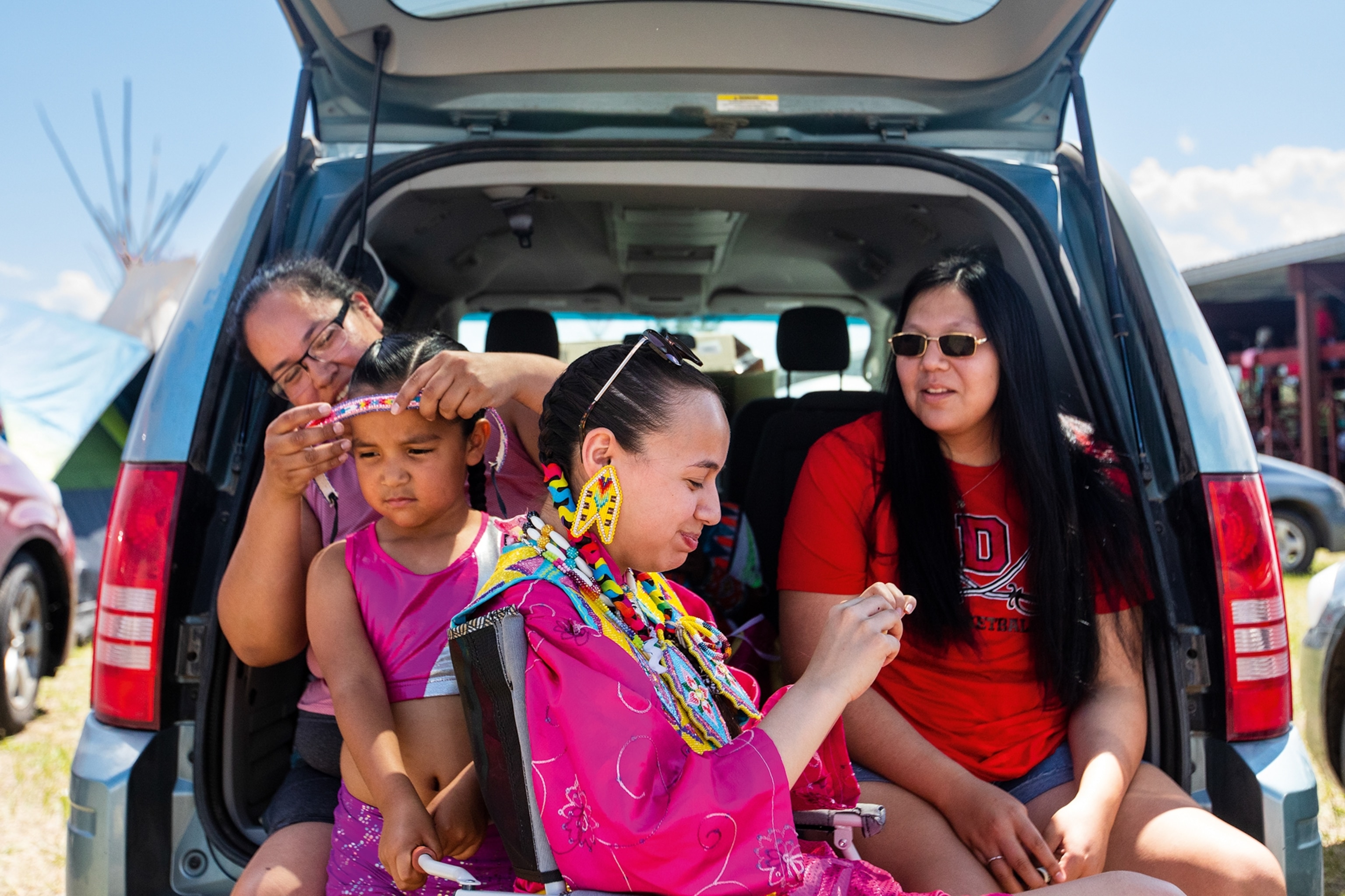 Two generations of women sat in the boot of their car as the older generation adds accessories to the younger ones.