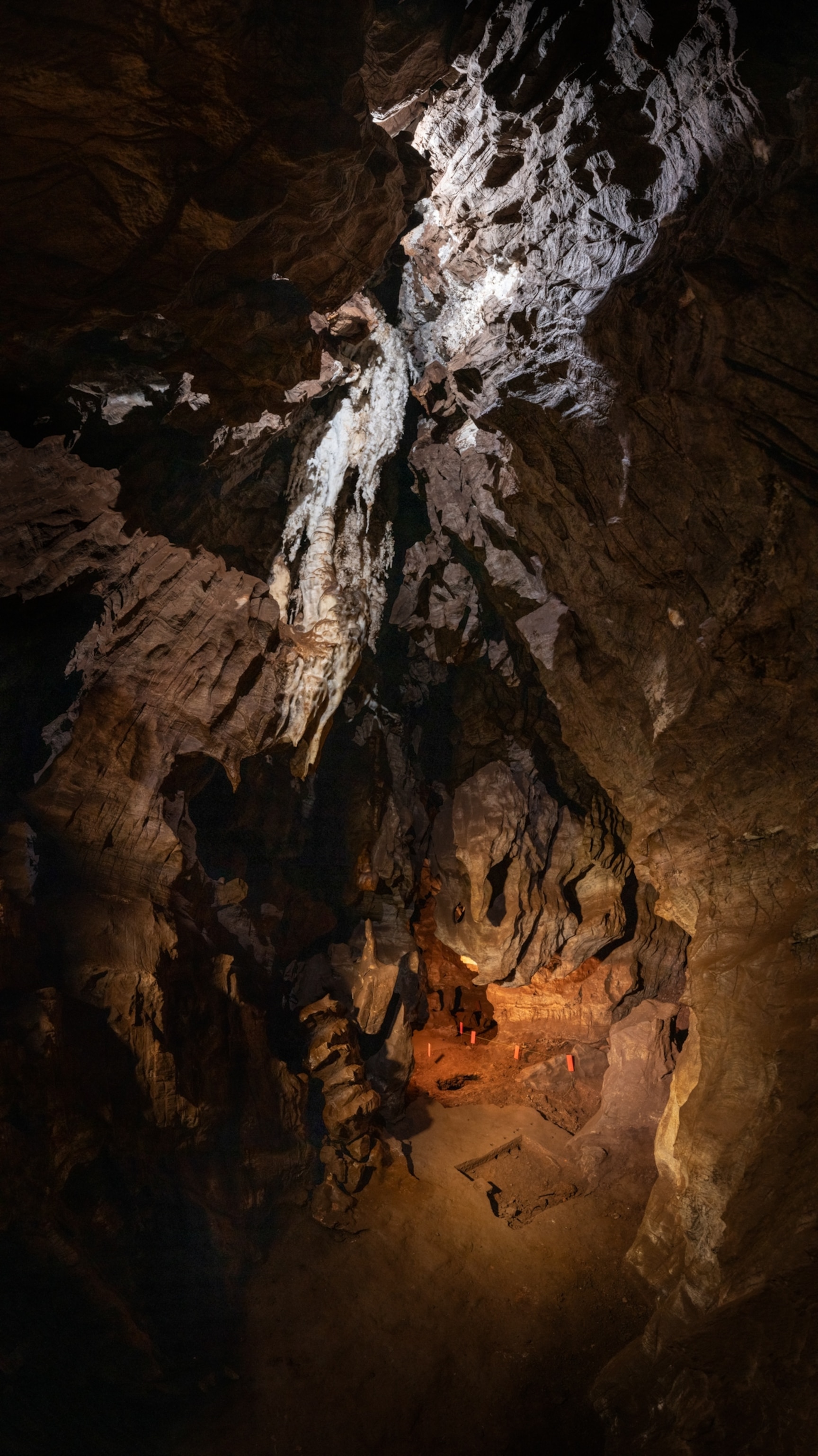 A vast, dimly lit cave with rugged rock formations. Light highlights the jagged ceiling