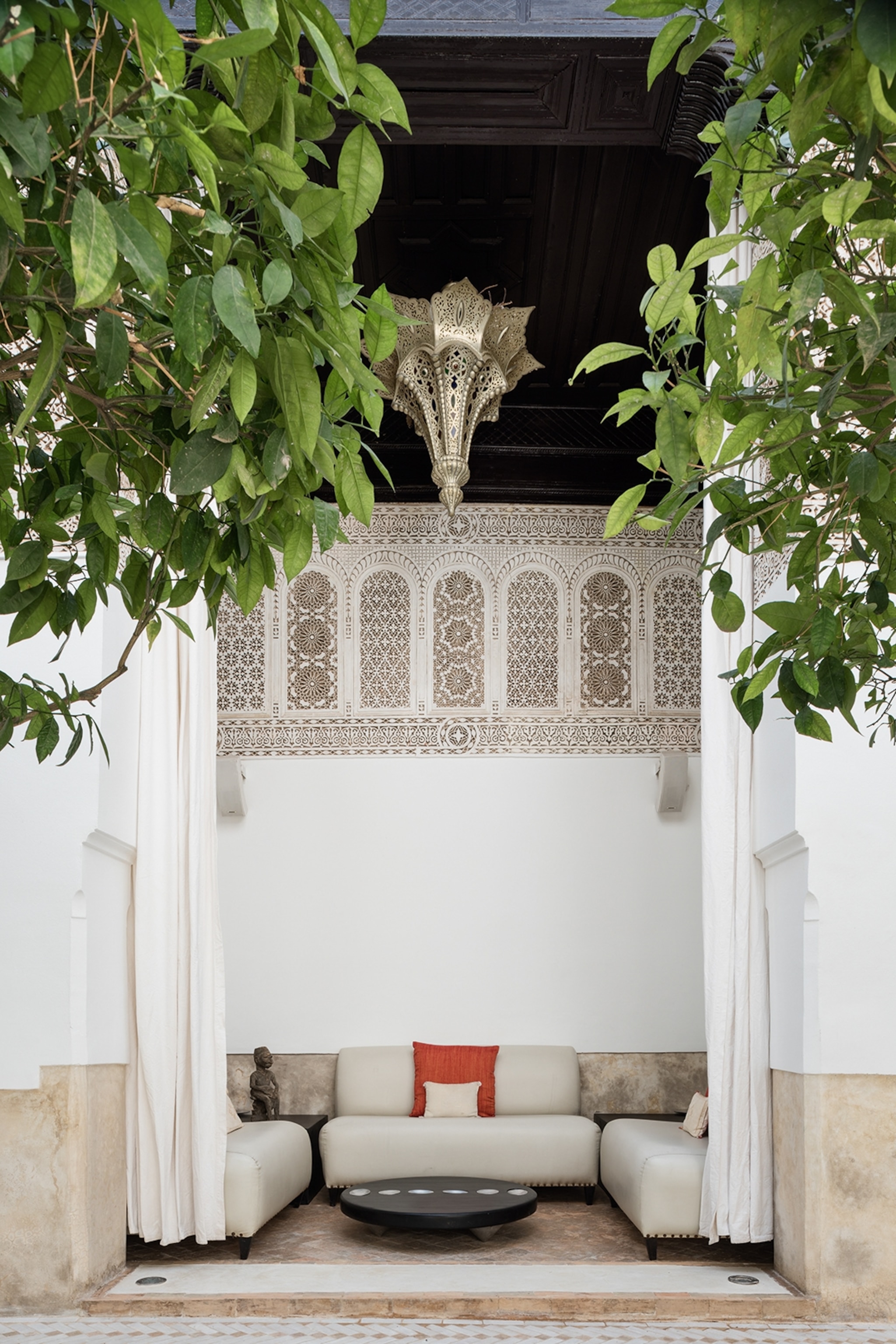 A tall seating corner in a marbled outdoor space with a curtain that could be drawn for privacy and a traditional Moroccan lamp hung above.