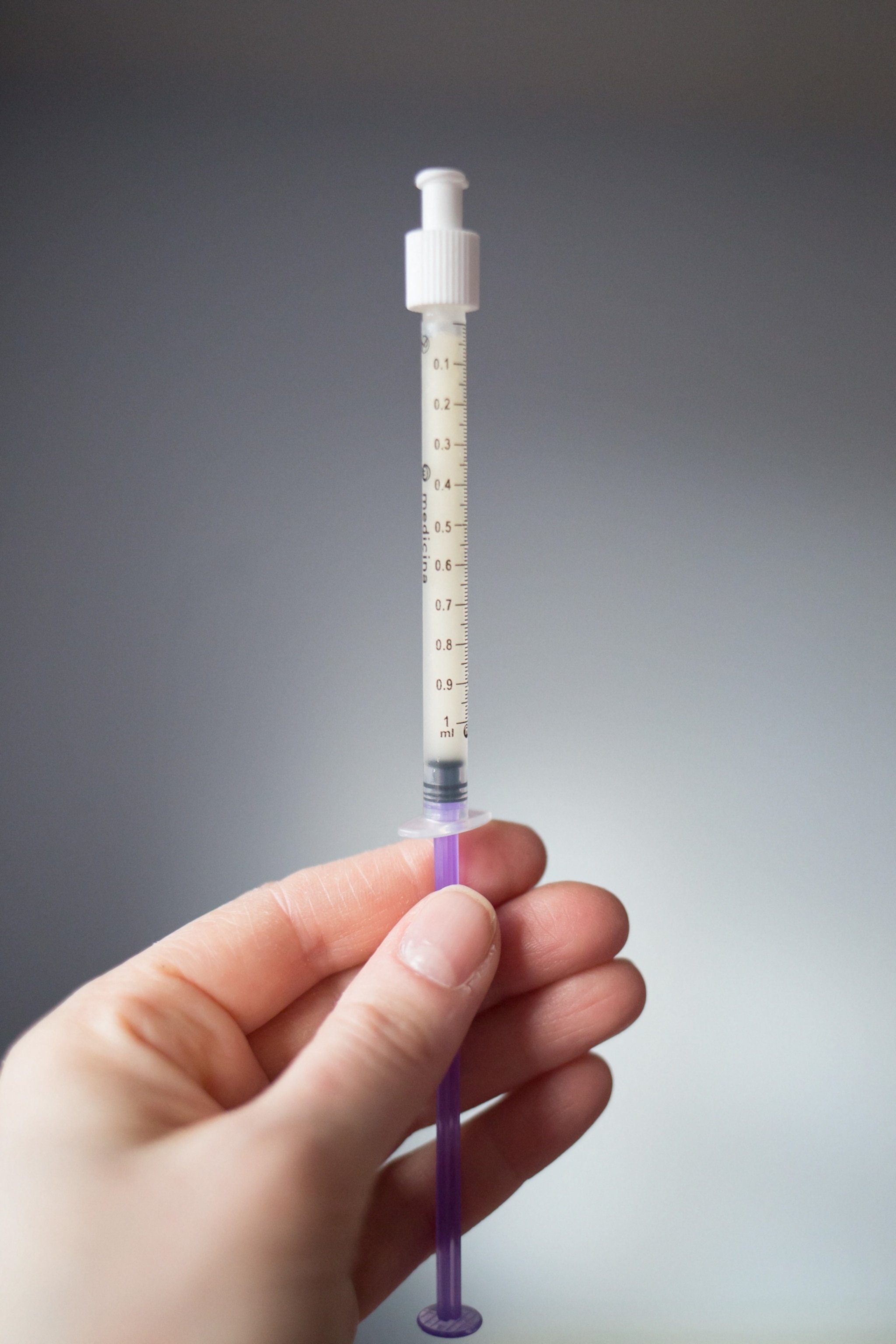 A hand holding a syringe containing a yellow-white, milky liquid, against a soft, neutral background.