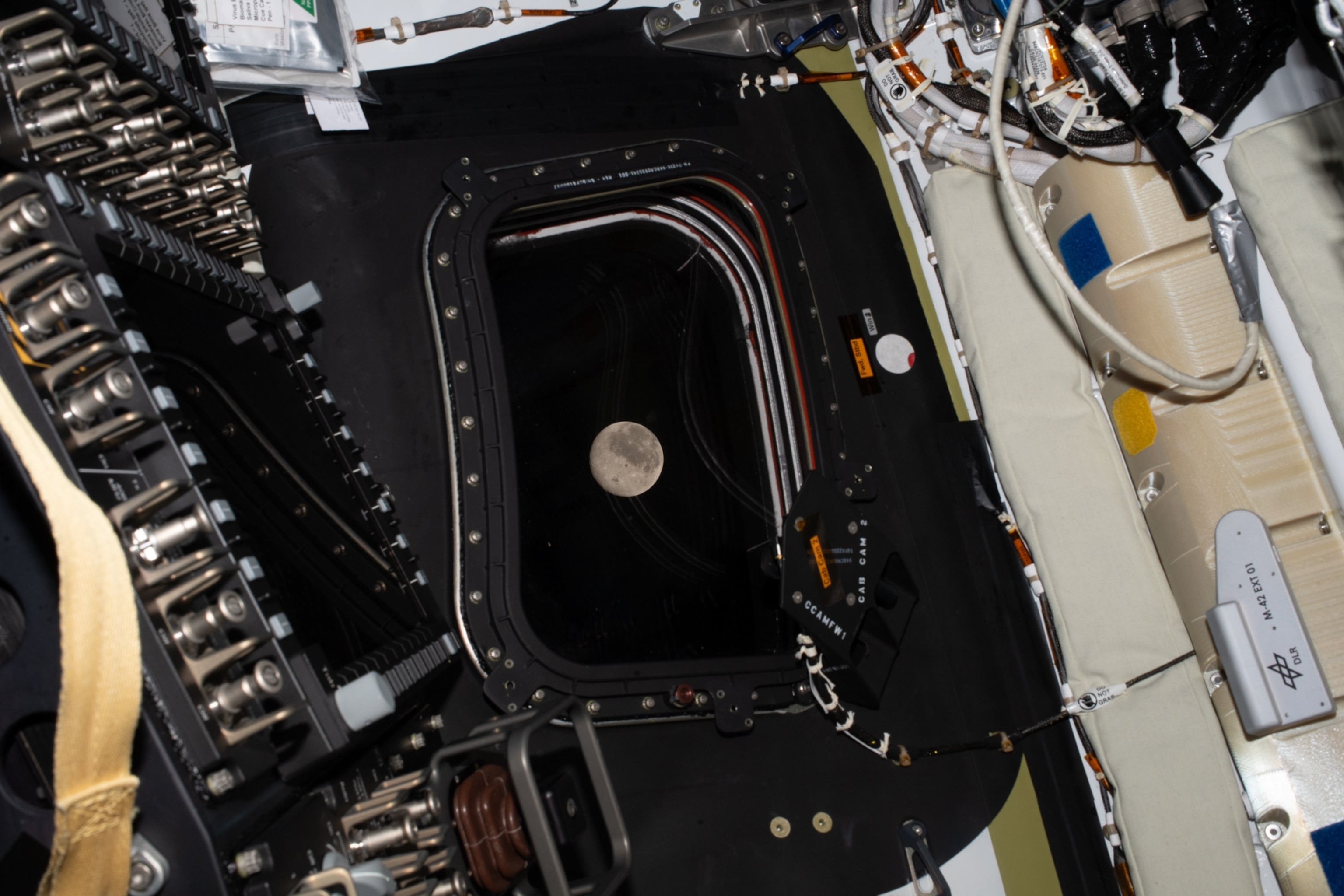 View of the moon from a spacecraft window, surrounded by intricate machinery and cables.
