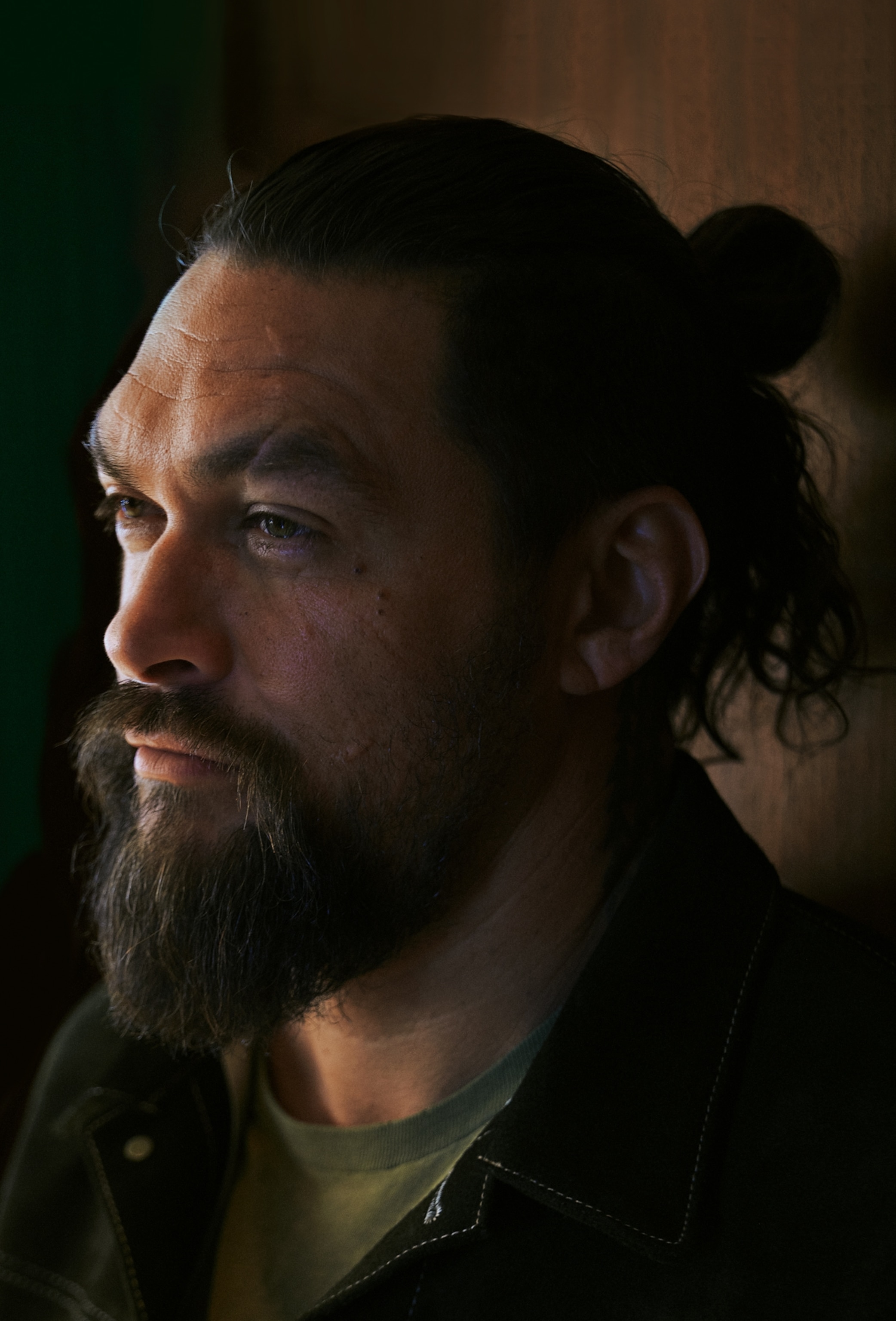 A man poses for a portrait against a wooden wall.