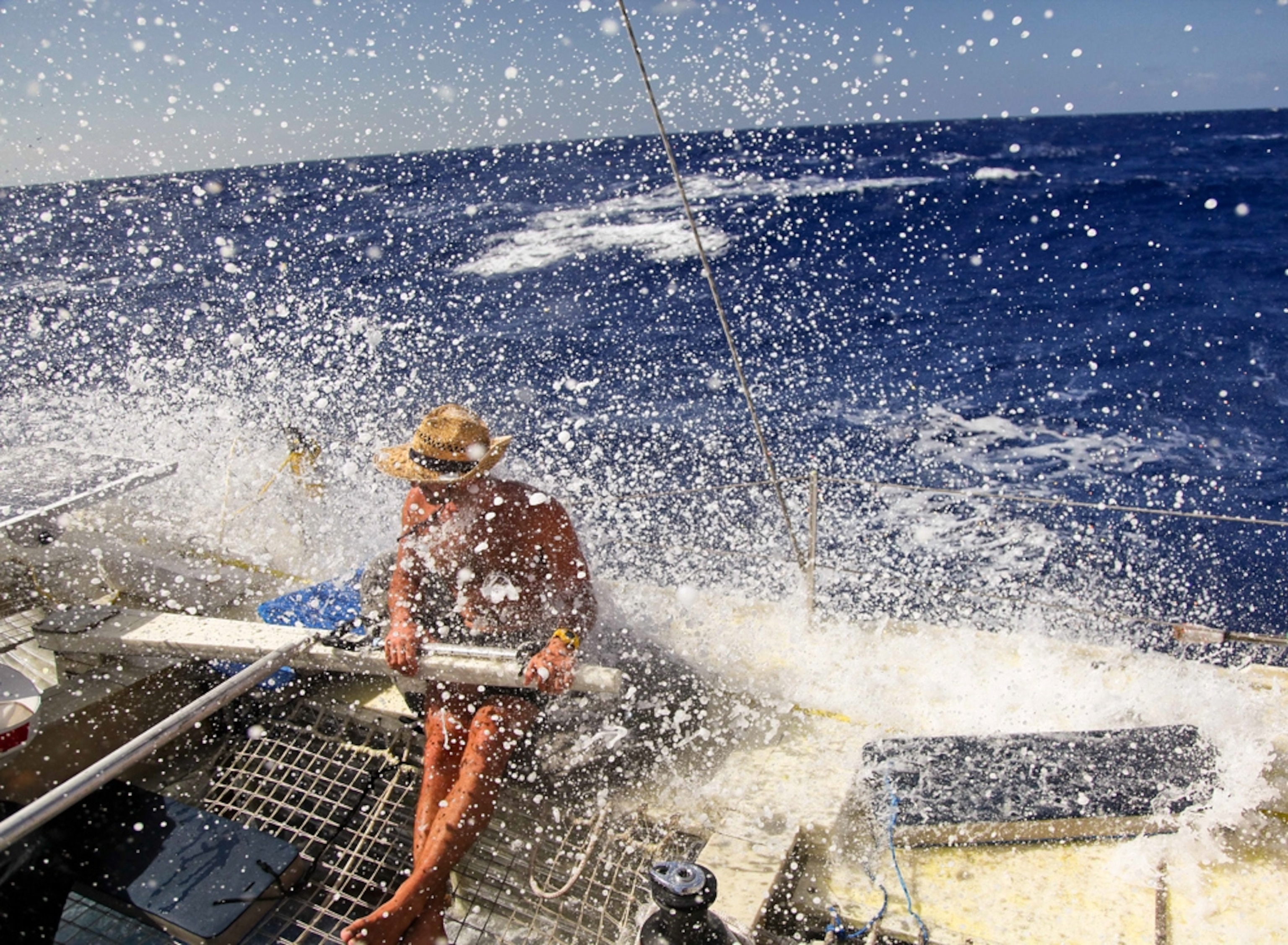 A sailor at sea is sprayed with a wave while aboard Plastiki