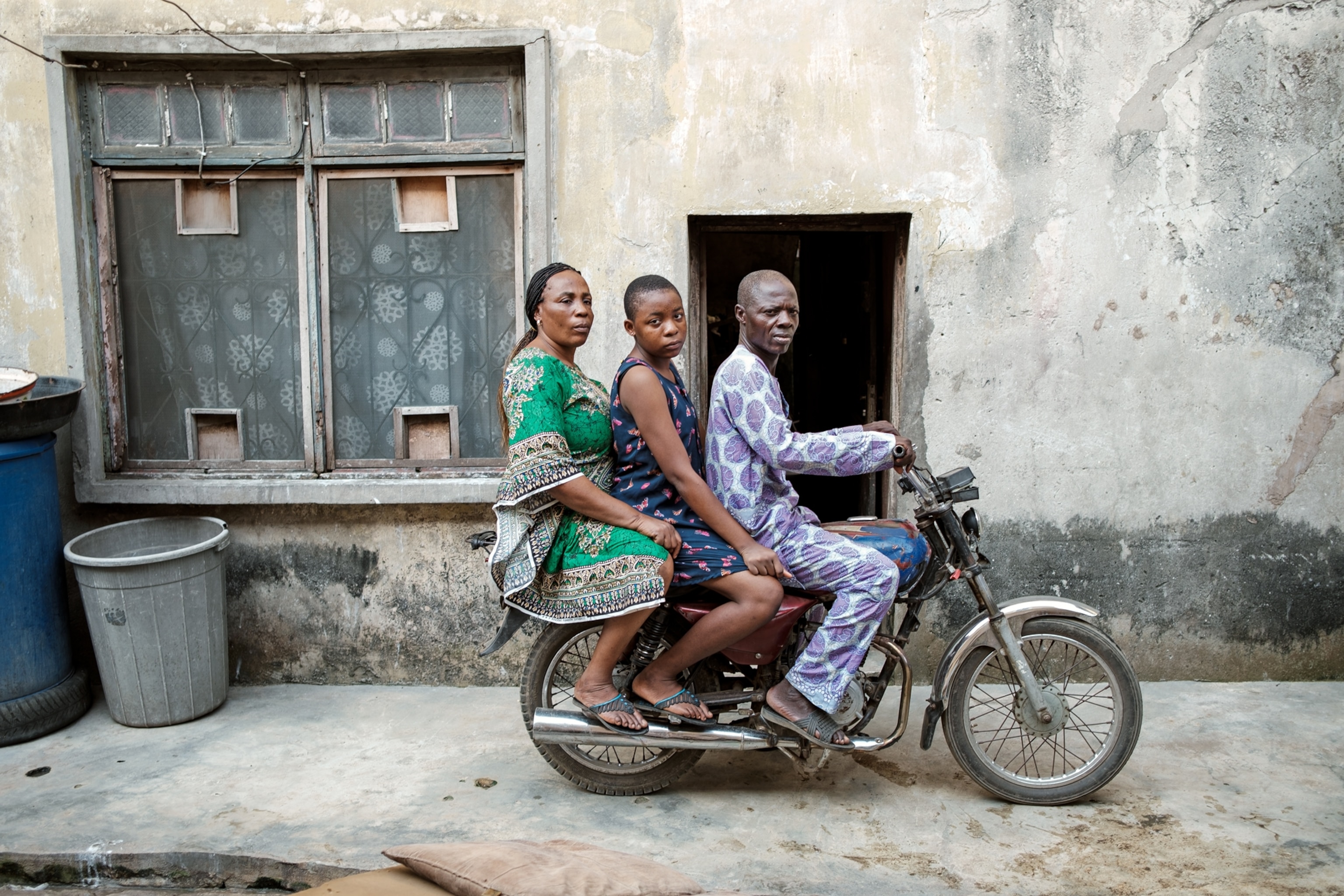 Man with wife and daughter on his motorbike looking into camera.