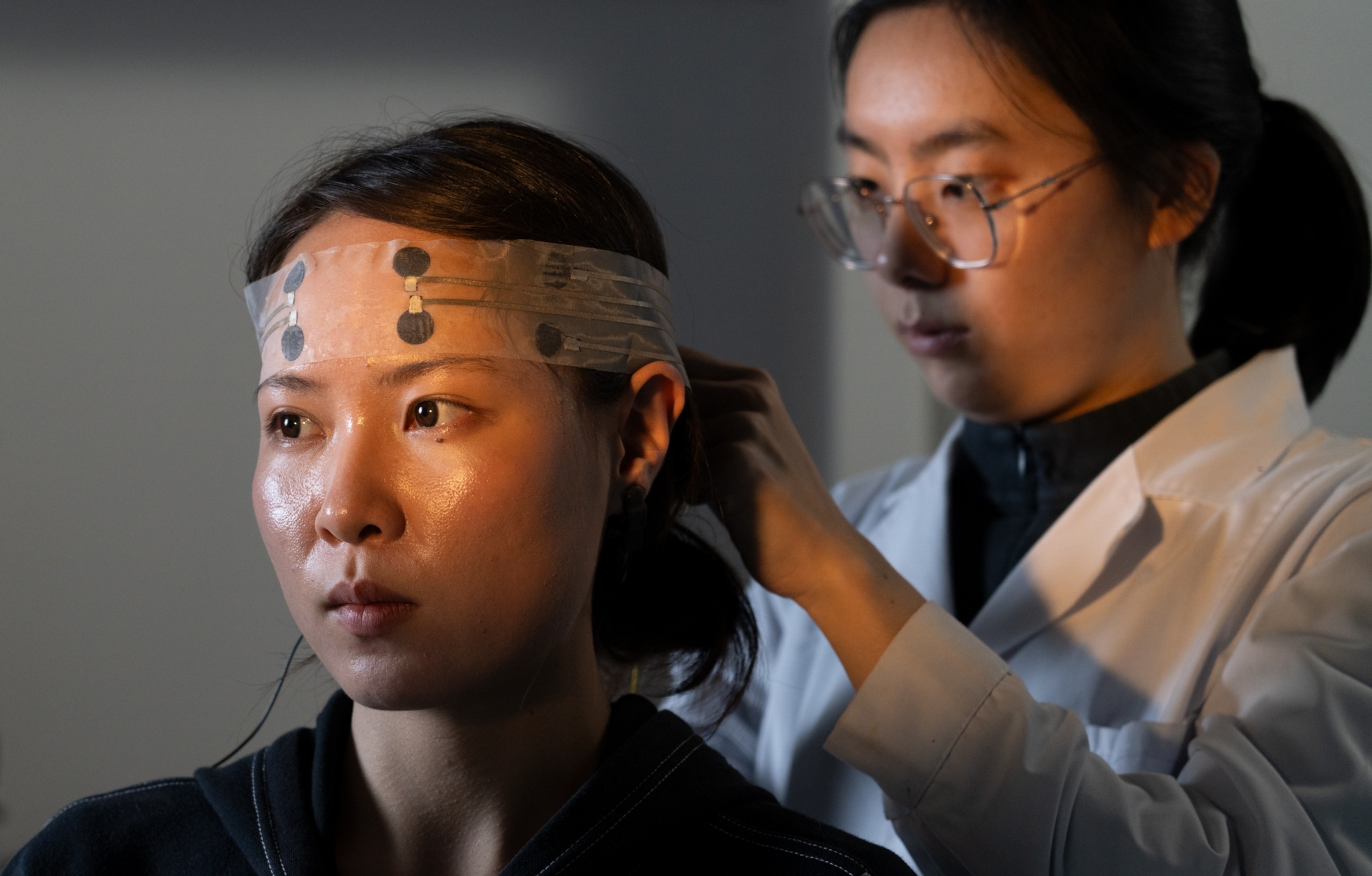 Women in lab coat attaching sensors to young woman's forehead.