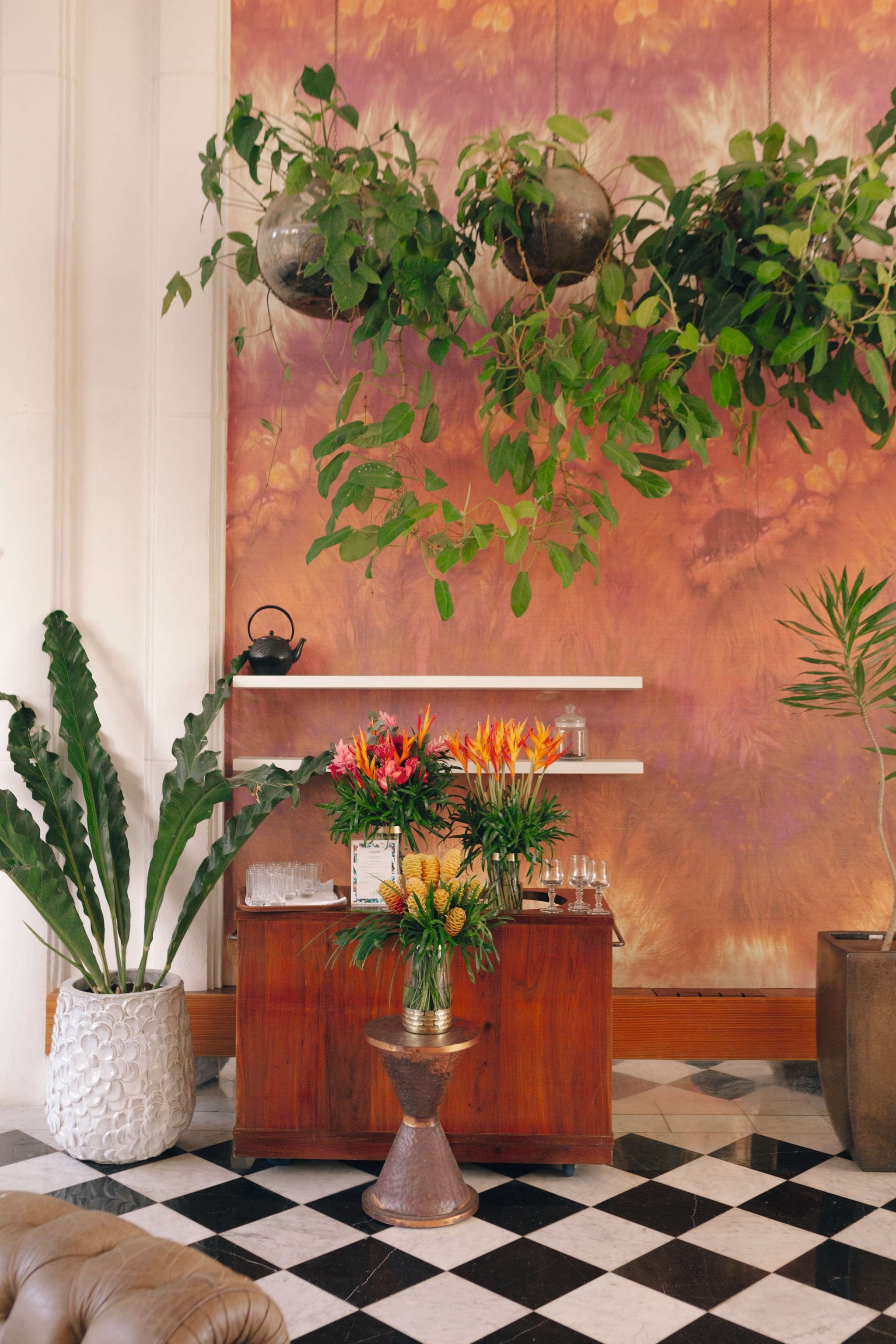 A small room with black and white marble flooring, terracotta coloured walls and decorated with greenery.