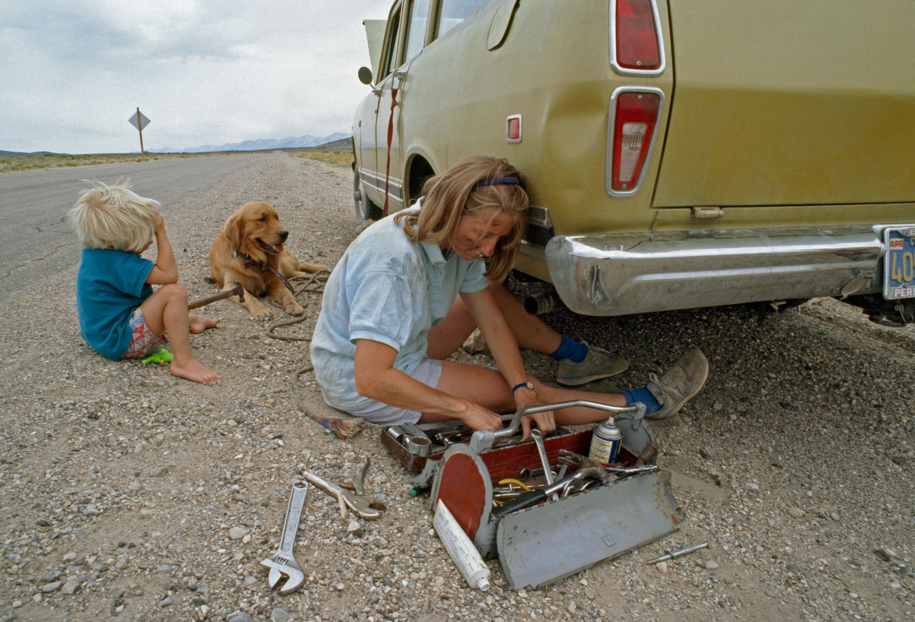 a woman fixing a car with child and dog present