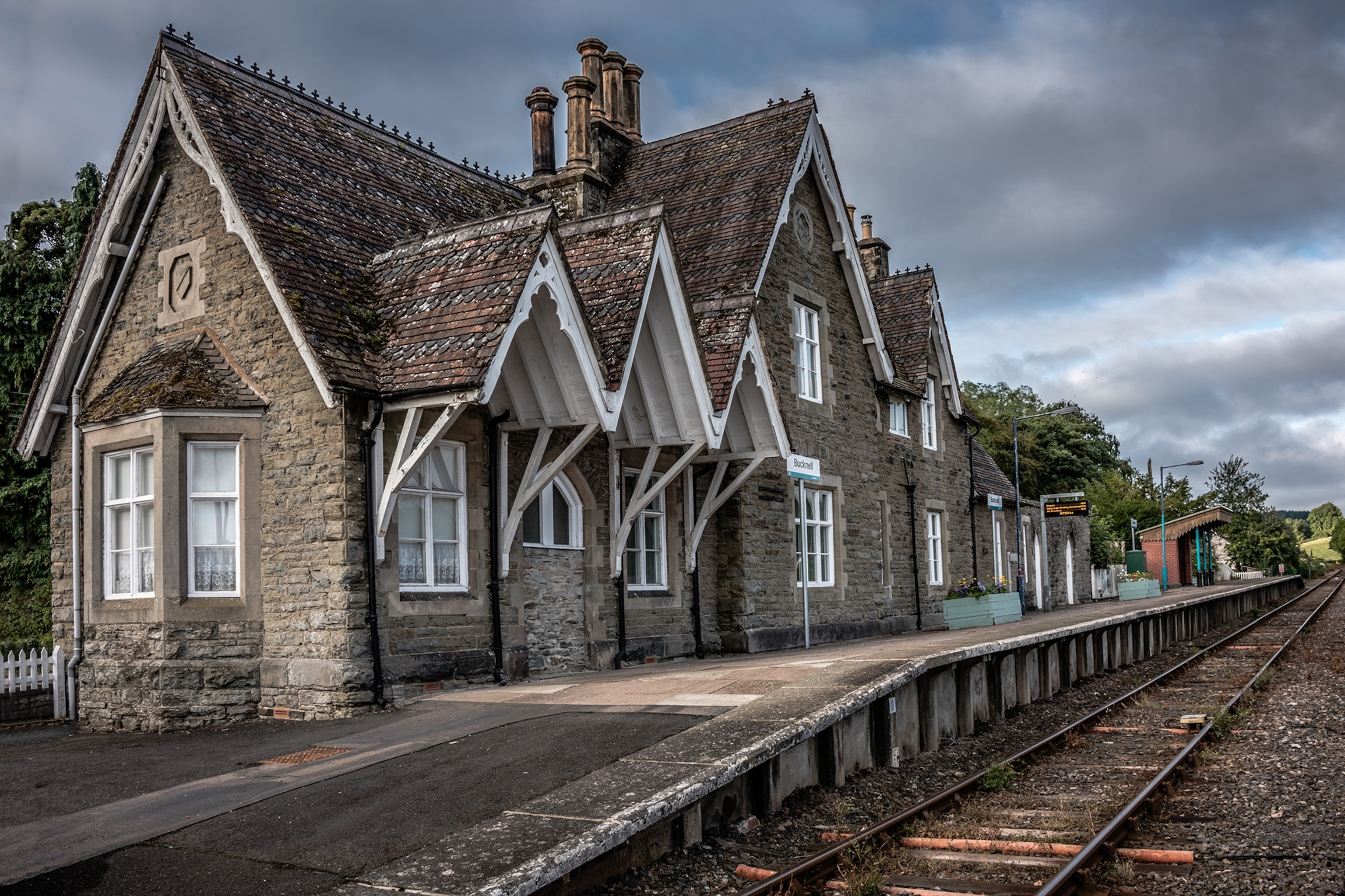 Brick station building at next to a short platform with rail tracks amd a cloudy sky