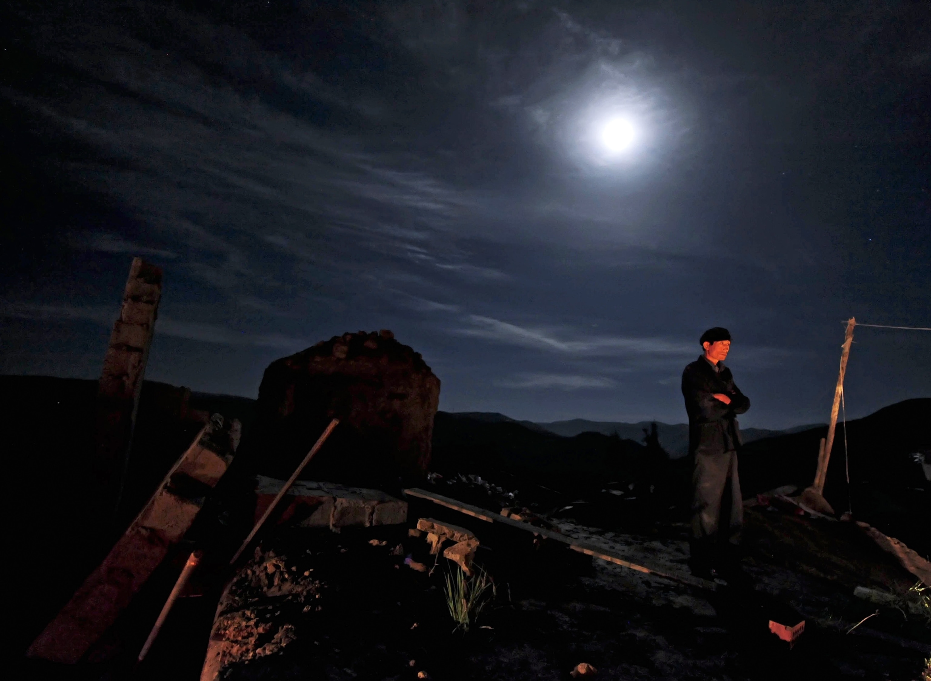 a man standing in the moonlight looking at earthquake destruction