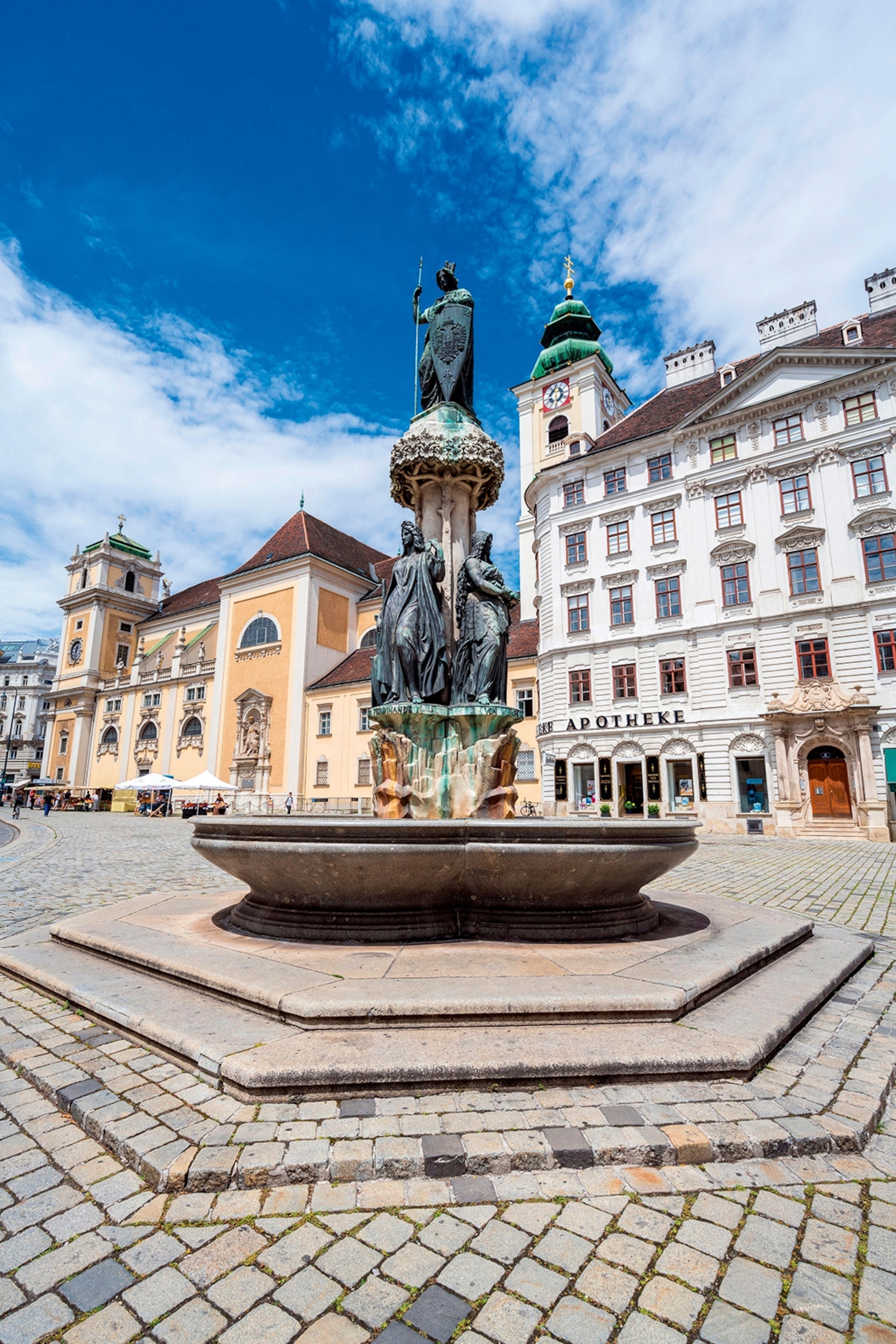 A plaza in Vienna with a fountain marked by an oxidised copper statue.