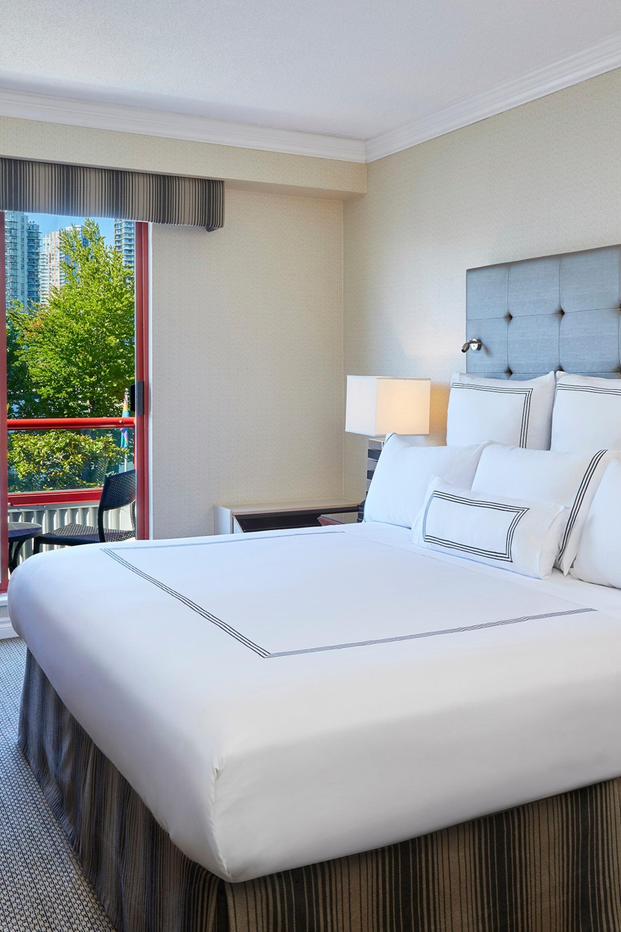 The interior of a simple hotel bedroom with queen-sized bed and views over the city skyline.