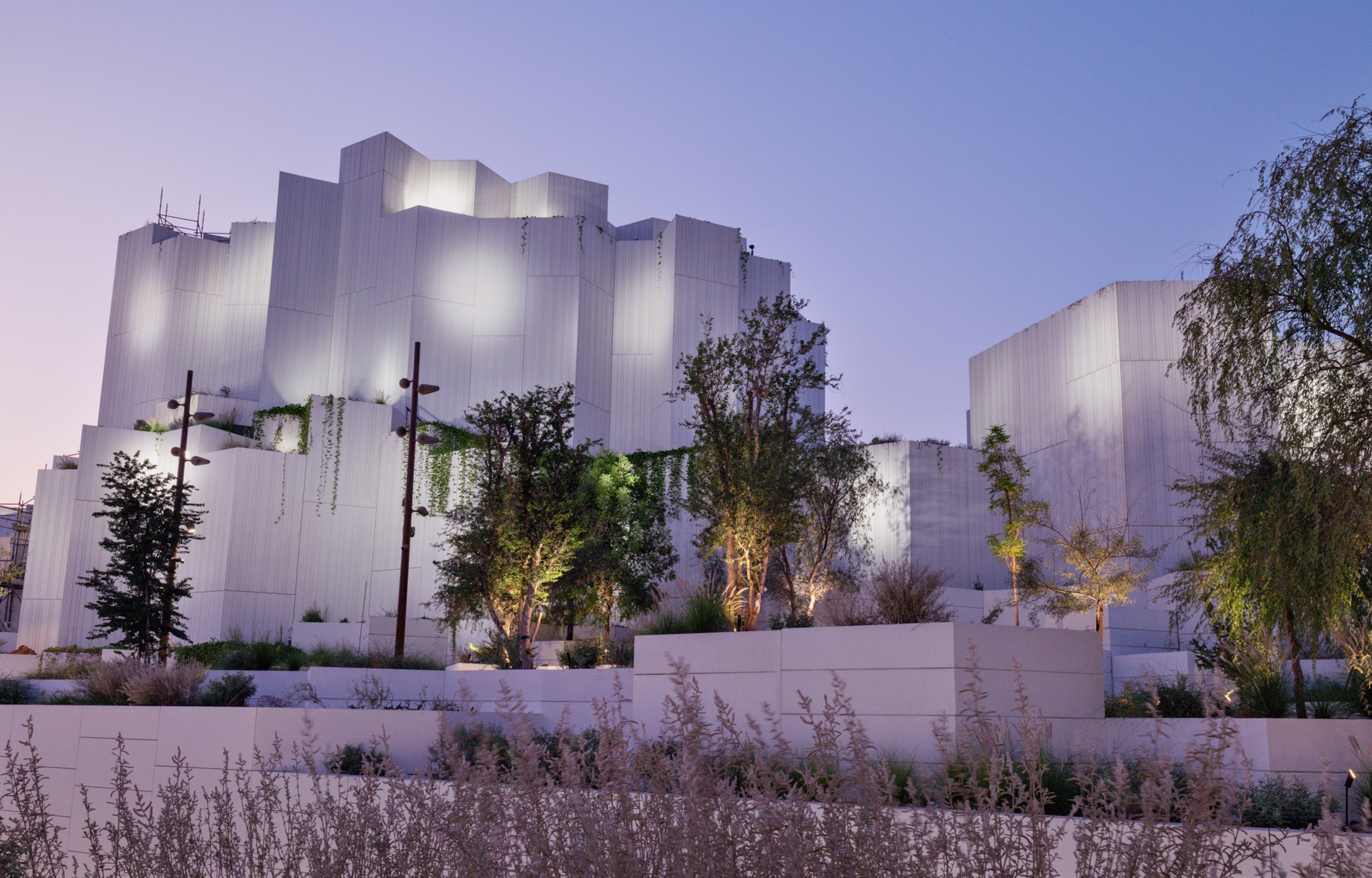Exterior of the natural history museum, which is a white, rock shaped building with multiple trees in front of it. It is dusk and the sky is turning a deep blue and purple.