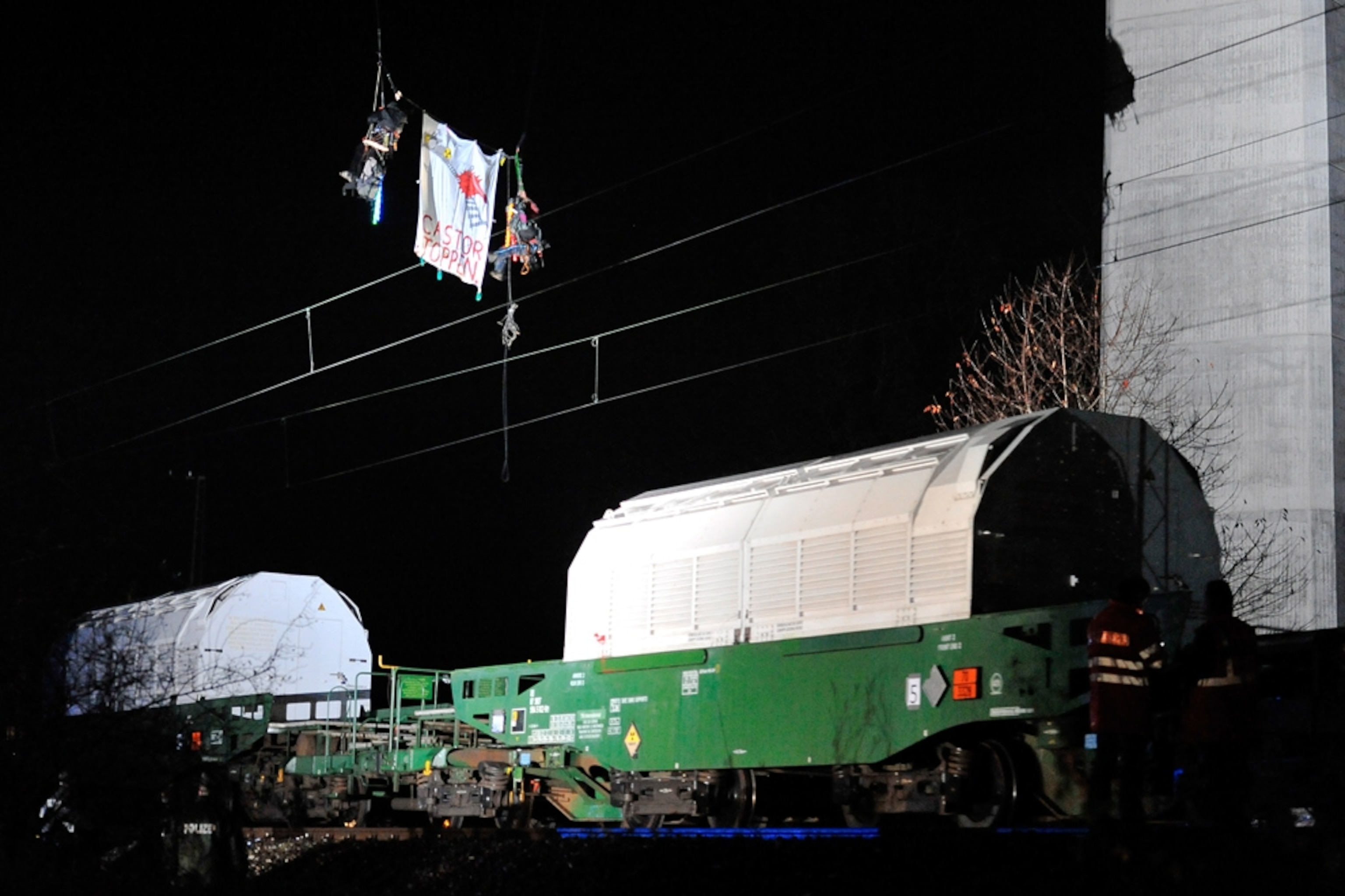 Two people dangle from a bridge, with a banner, and hang high above a passing nuclear-waste train (picture)