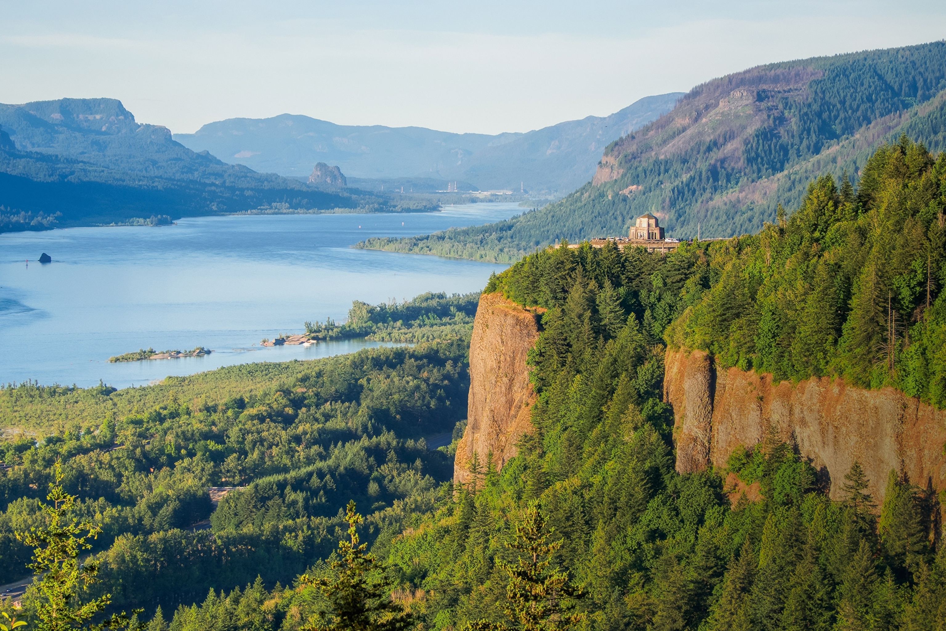 A landscape shot of an observatory towering over a wide river gorge surrounded by forested hills.