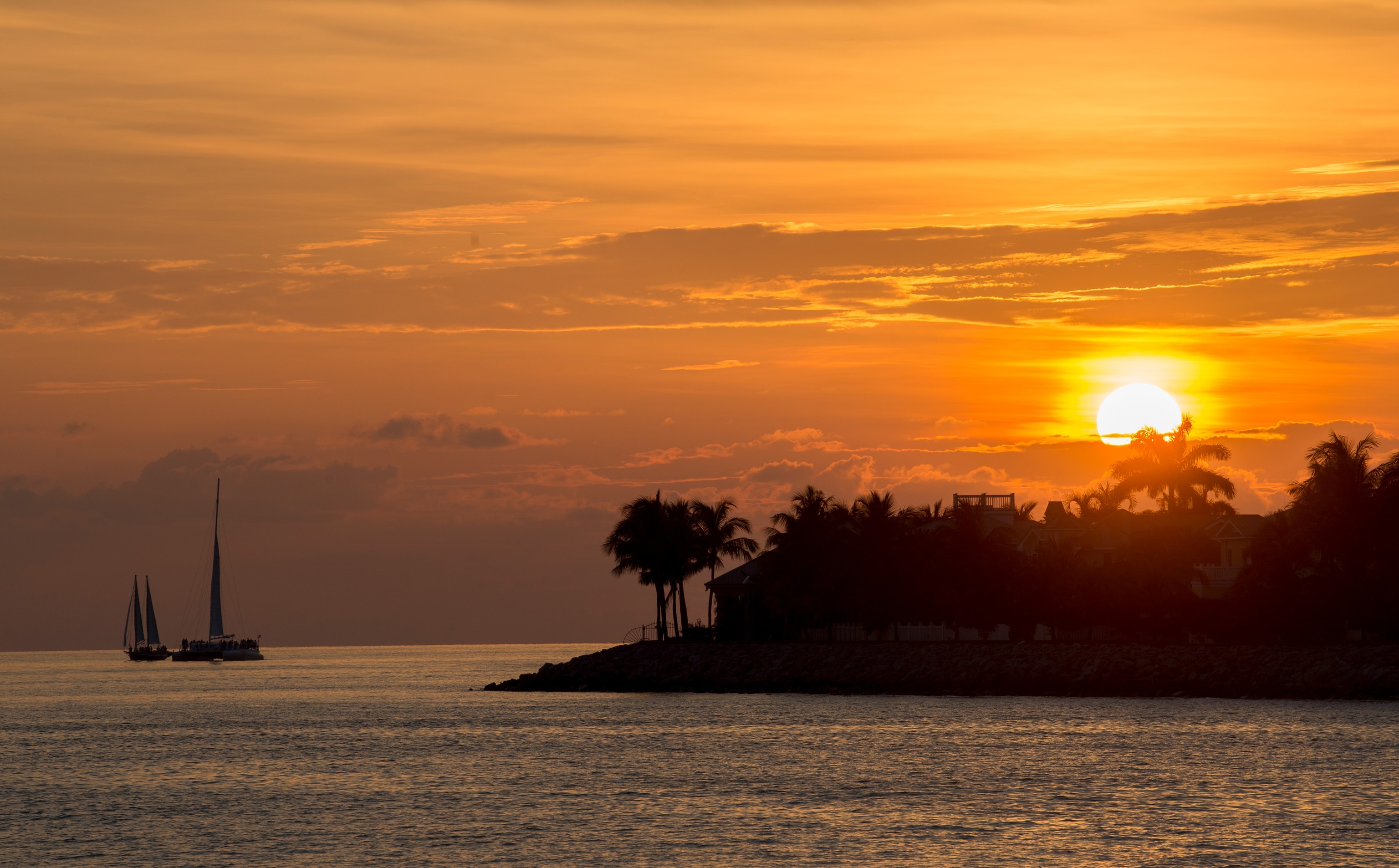 A large orange sun on the horizon behind sailboats in Key West, Florida.