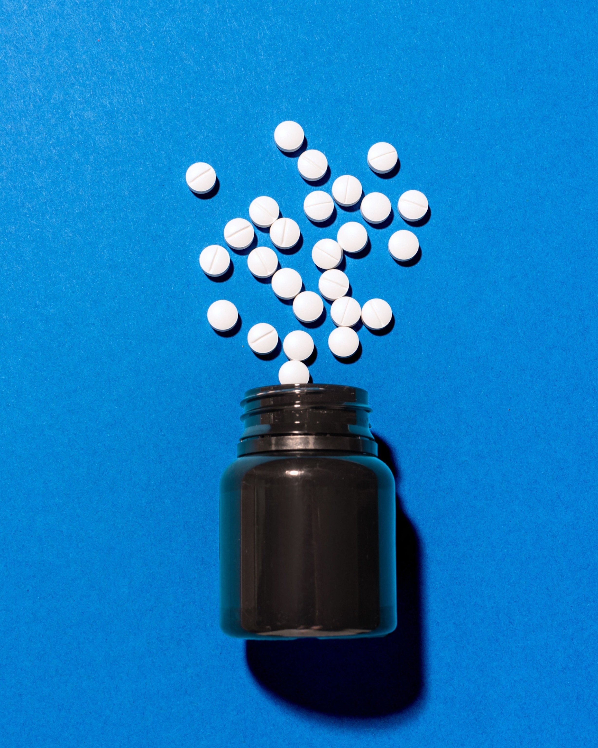 A black bottle with white tablets scattered above it against a vibrant blue background