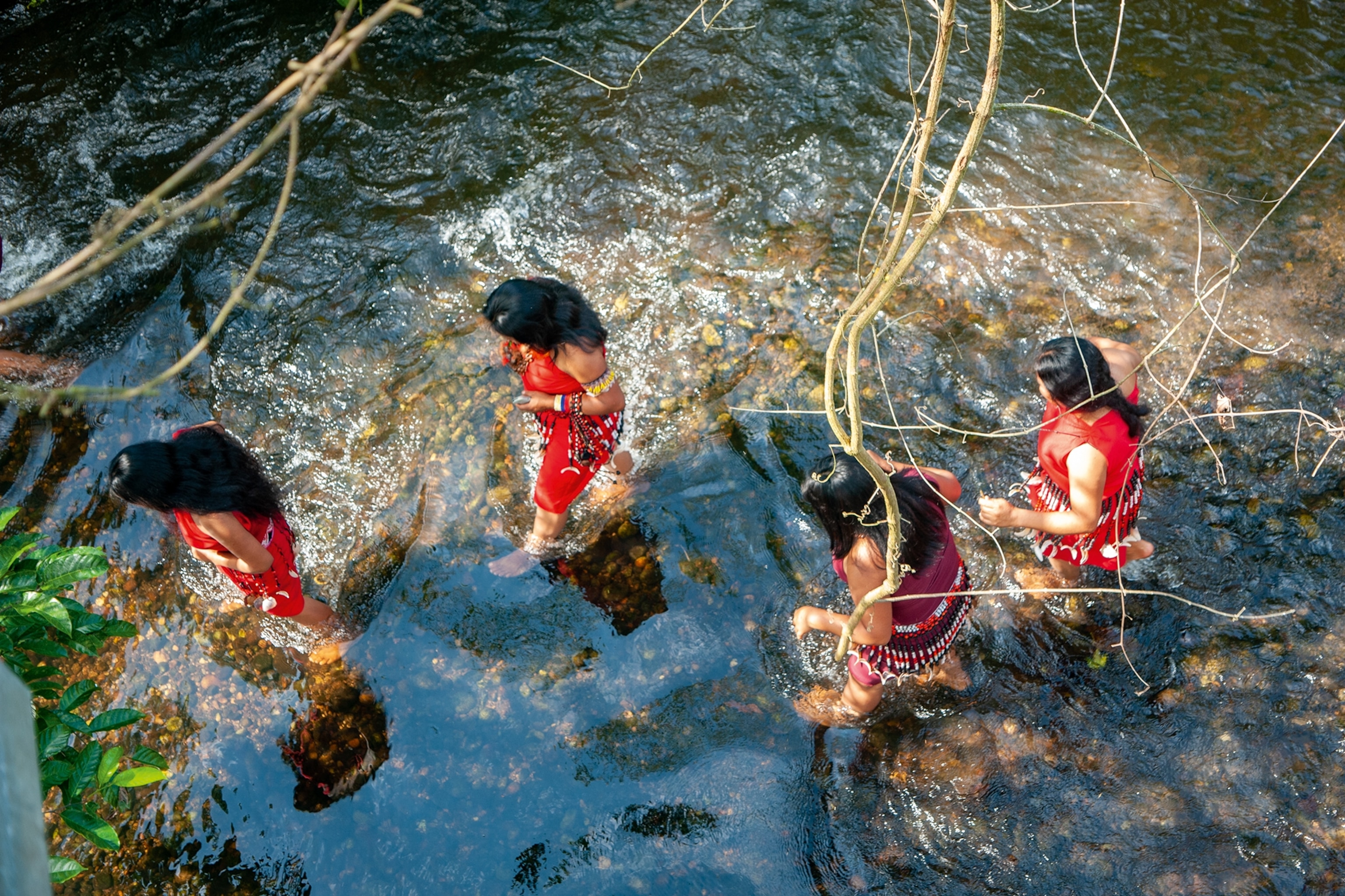 A group of women wading through a river, shot from above.