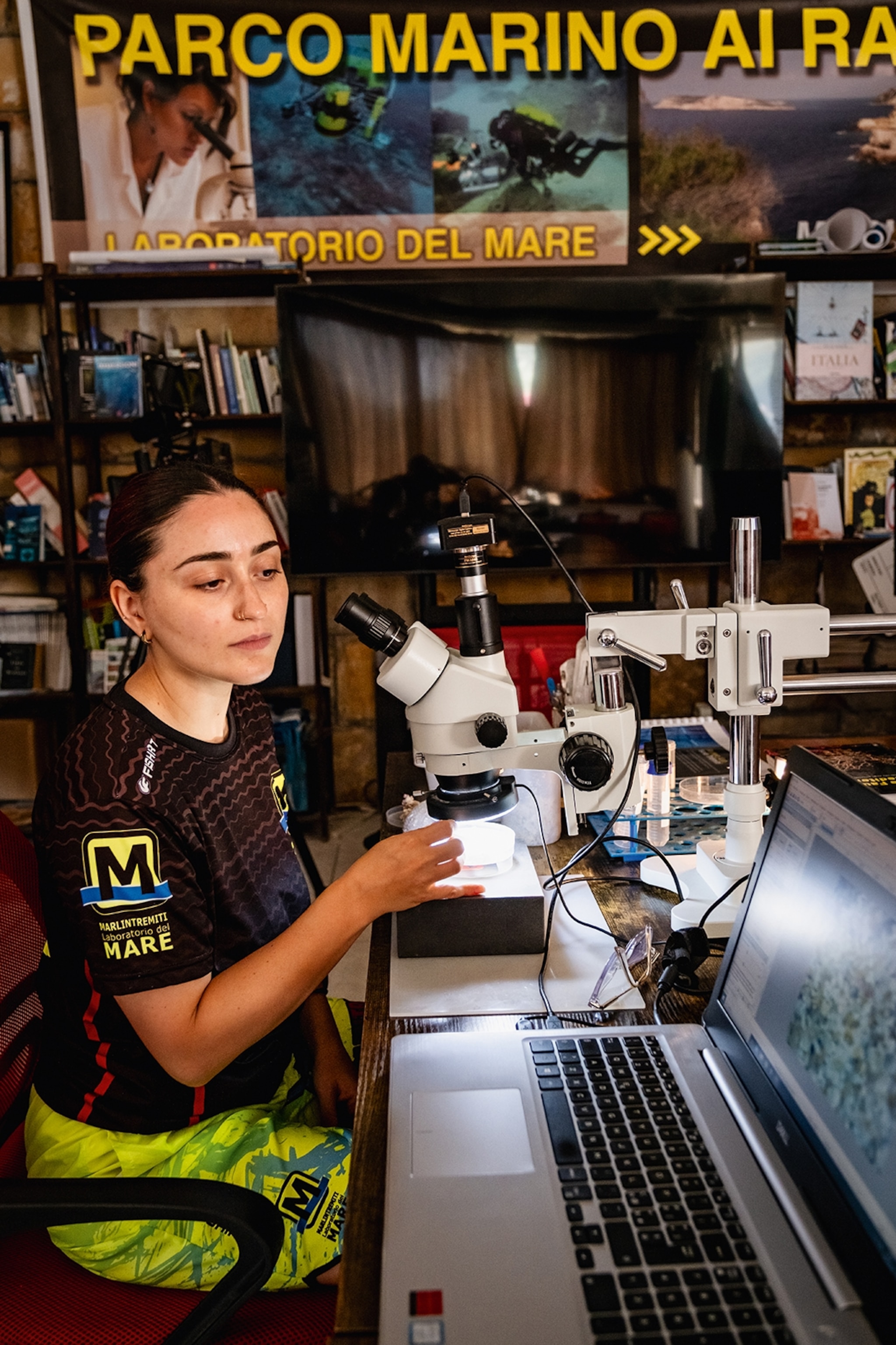 A young female marine biologist examining a probe under a microscope in a lab.