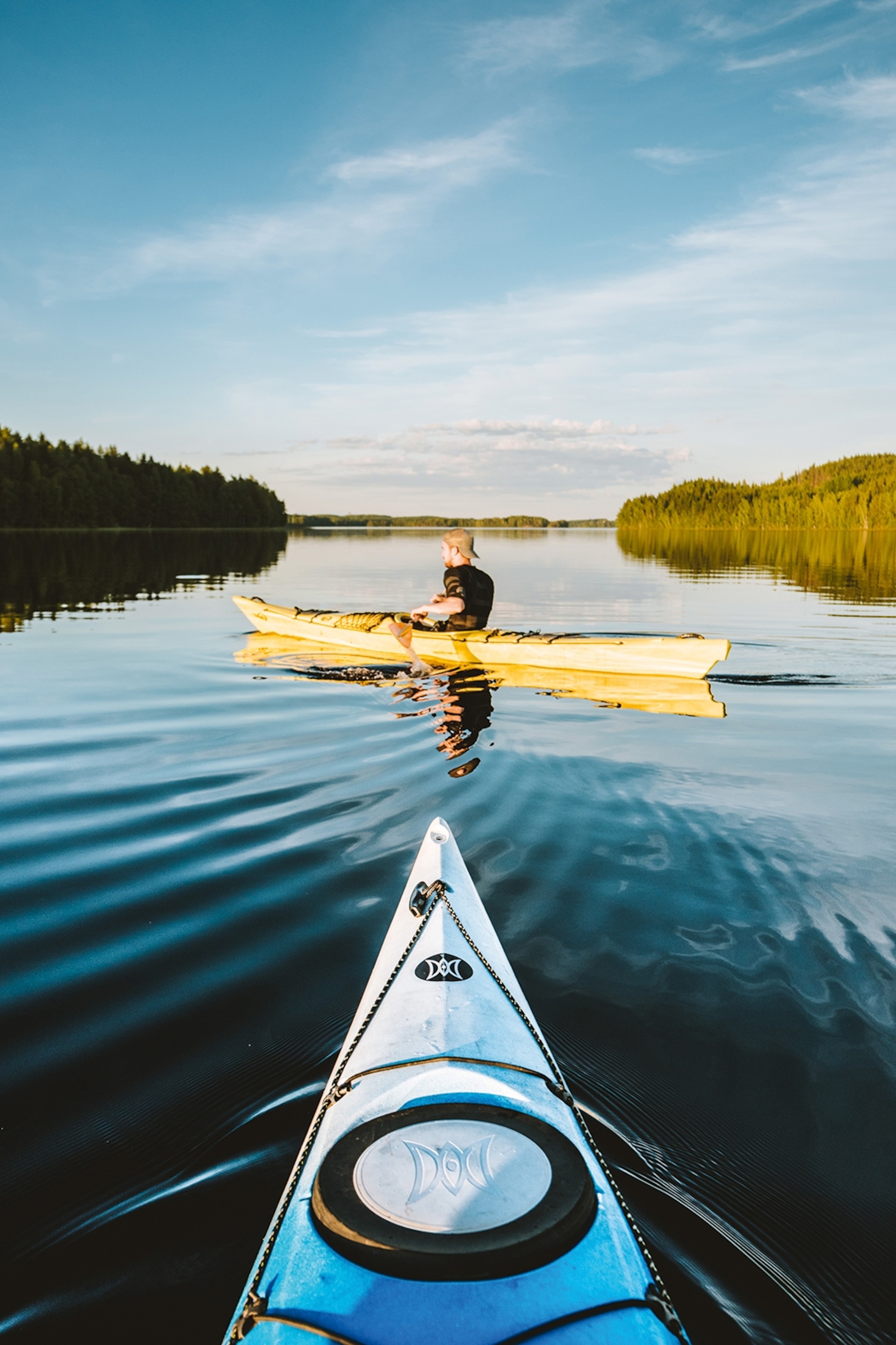 A POV perspective from someone in a kayak as another friend in a kayak is leading the way across a lake.