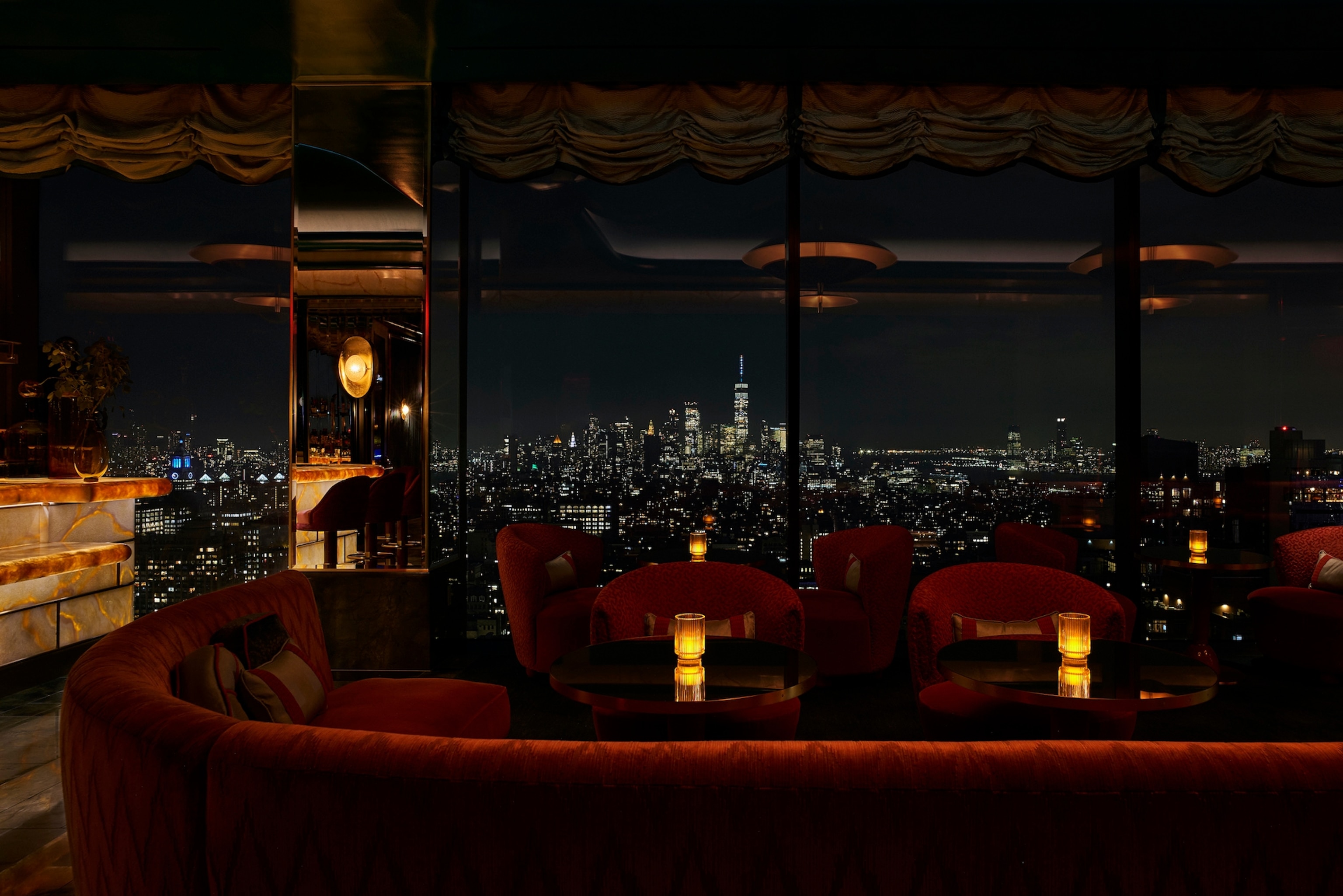 A sleek and dimly lit rooftop bar with panorama views over NYC and velvet armchairs.
