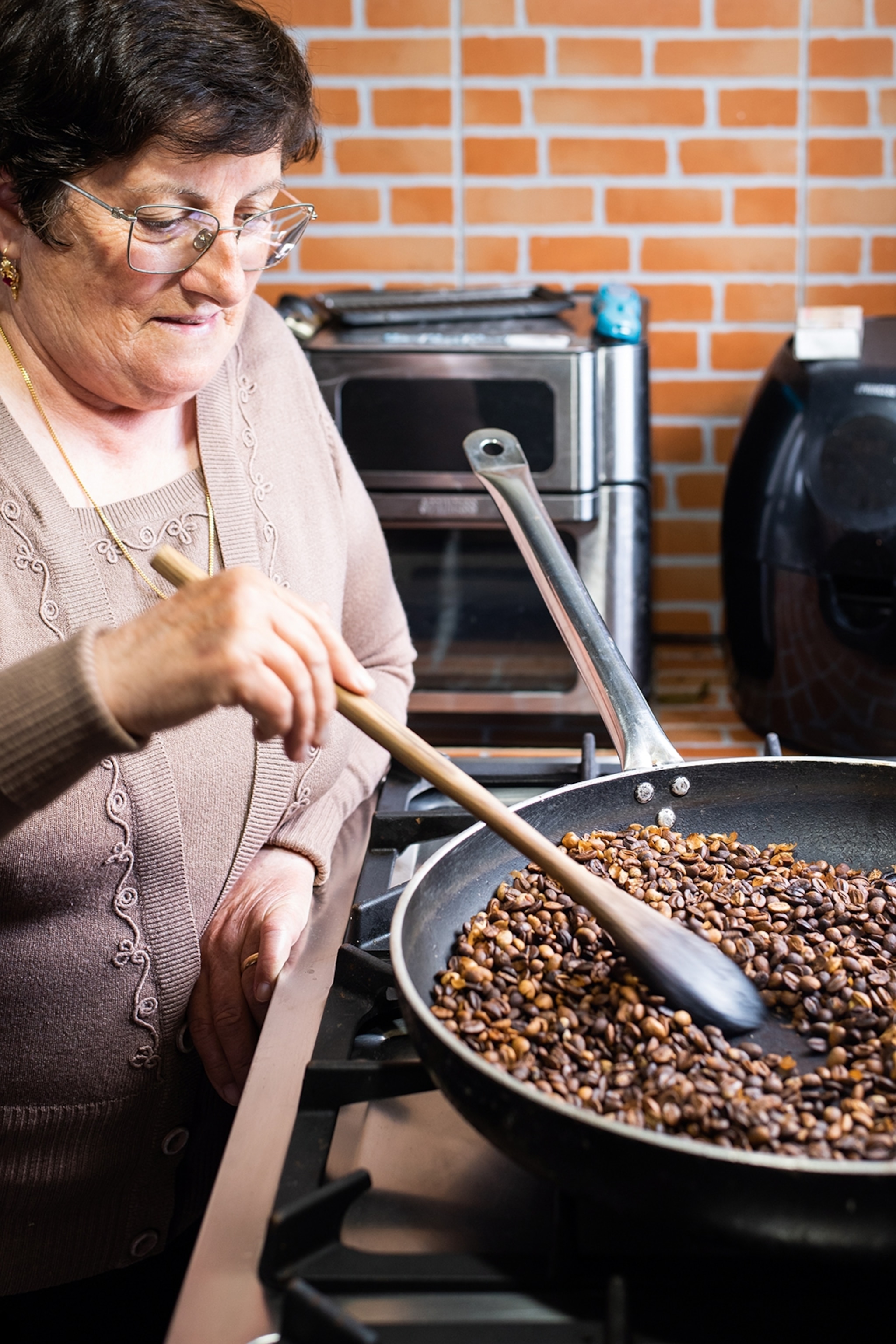 An elderly woman stirring a pan of coffee beans.