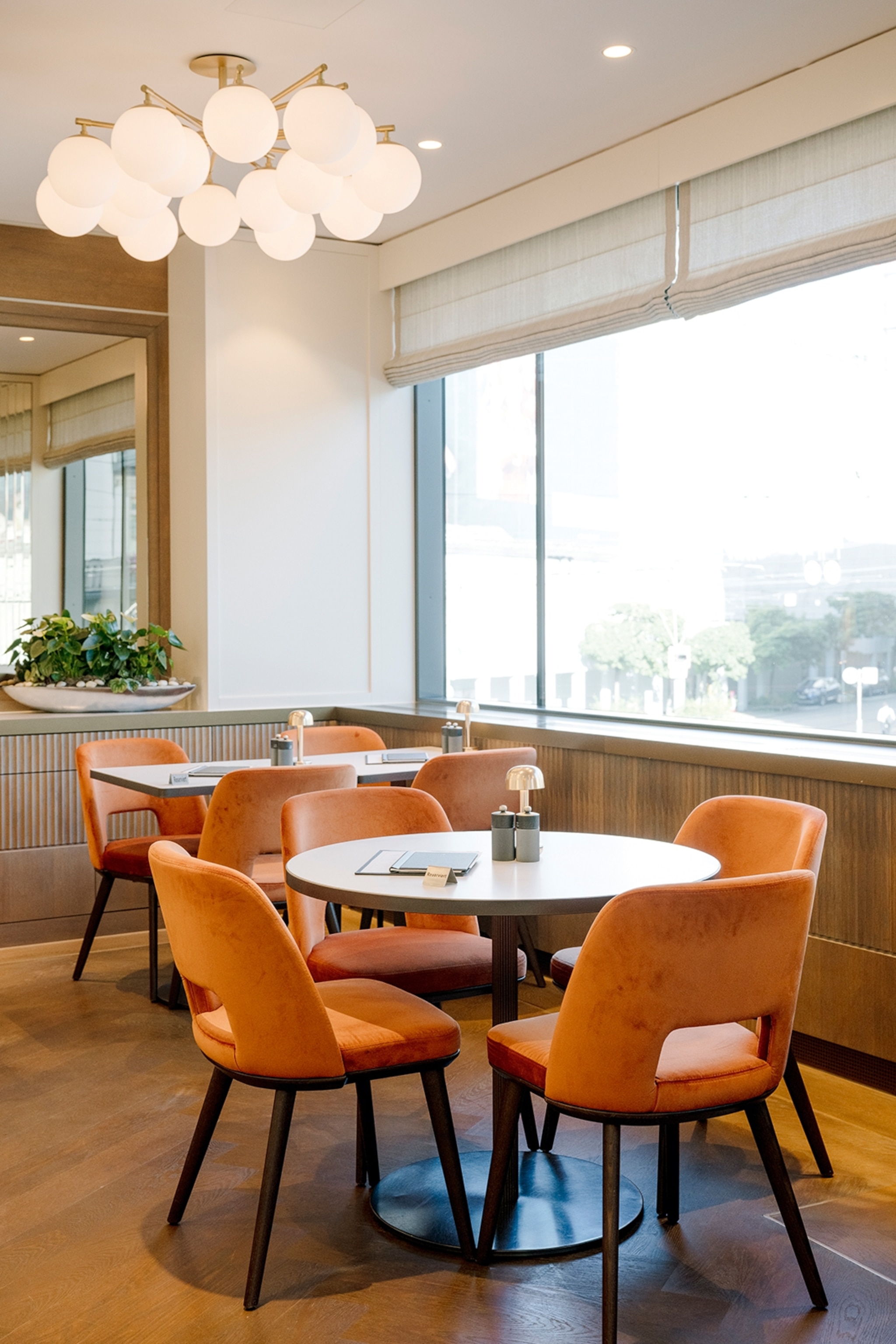 The modern interiors of a patisserie with soft velvet chairs at round tables.