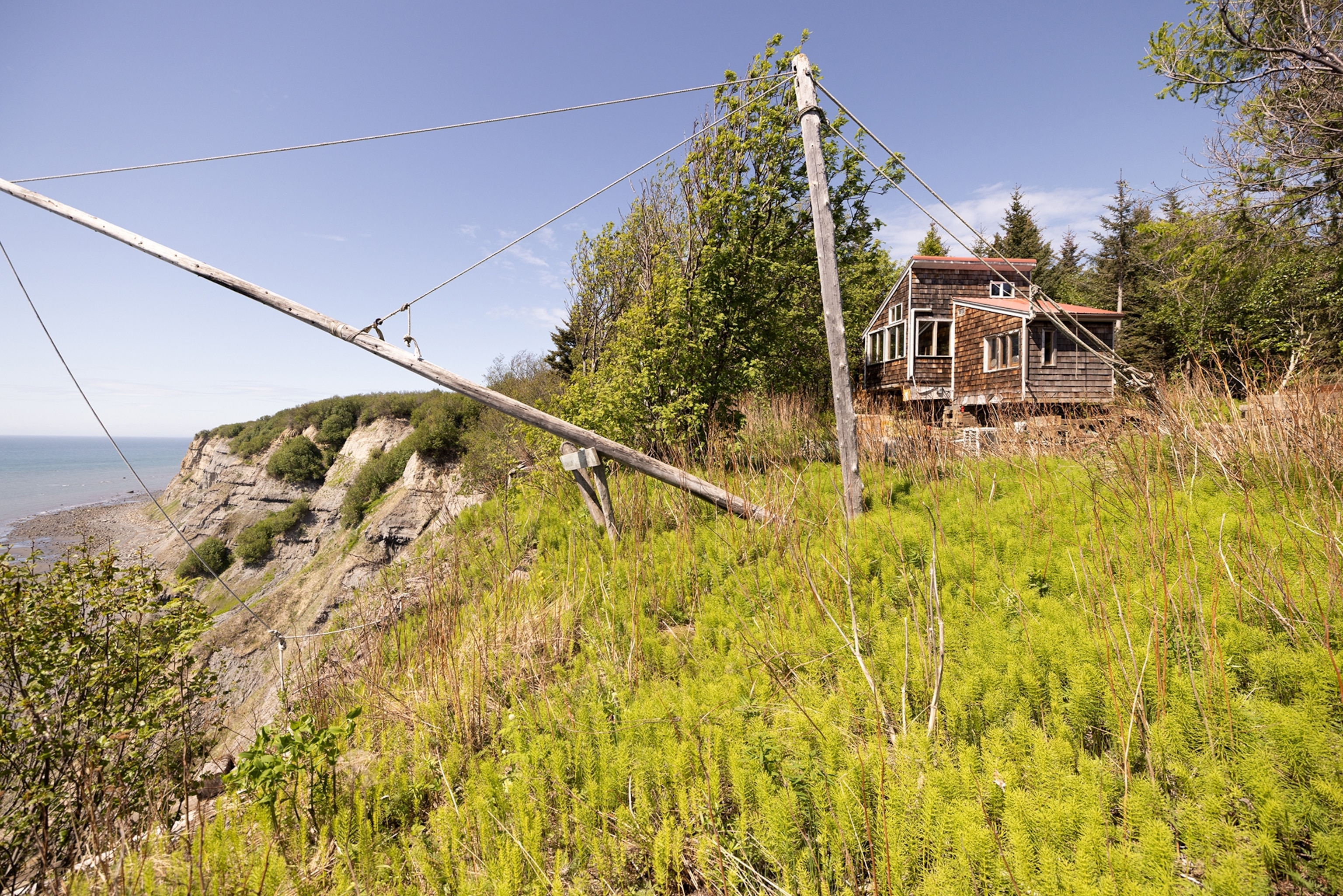 A wooden house surrounded by trees sits near the edge of a steep cliff.