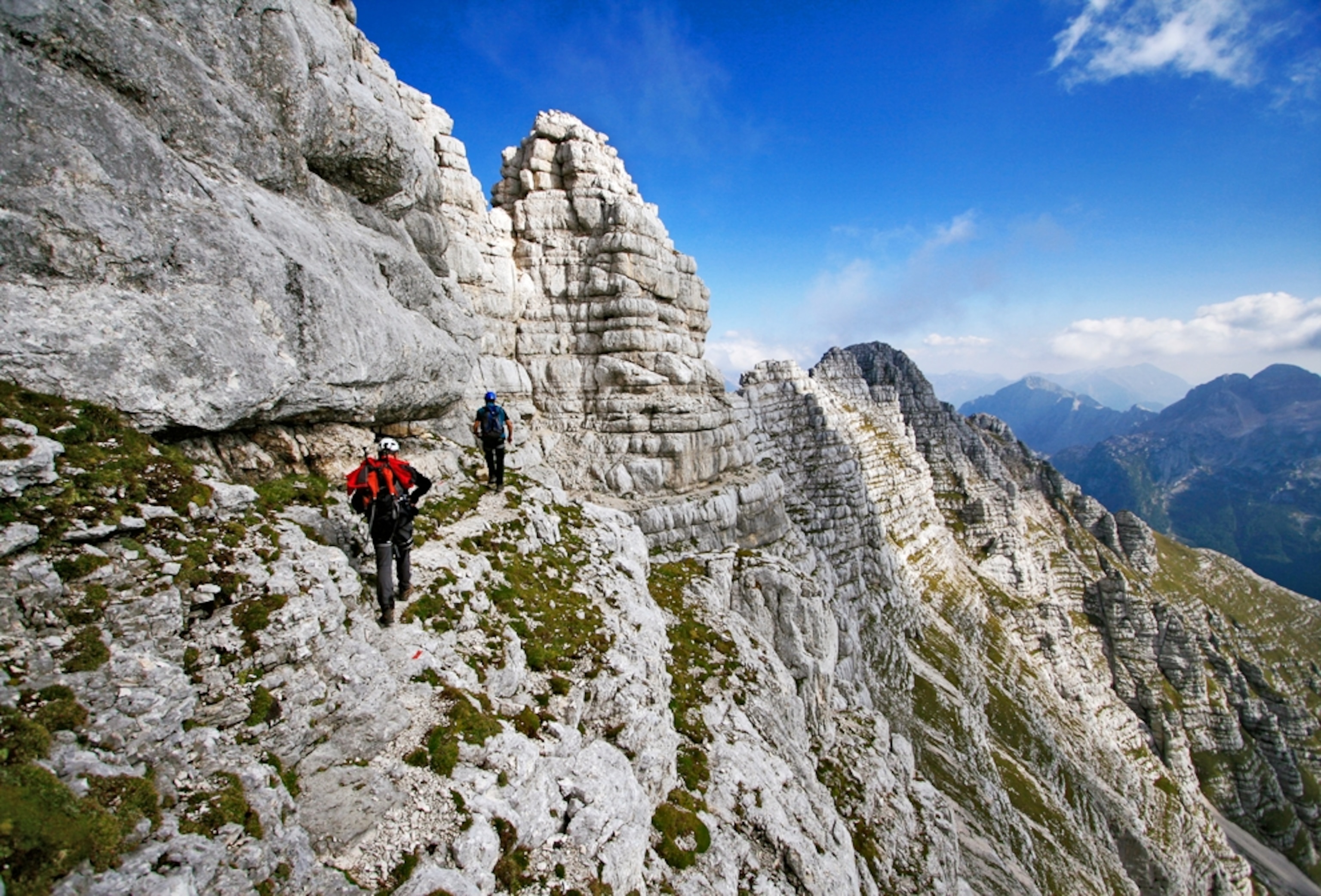 Two hikers walk along the side of a mountain