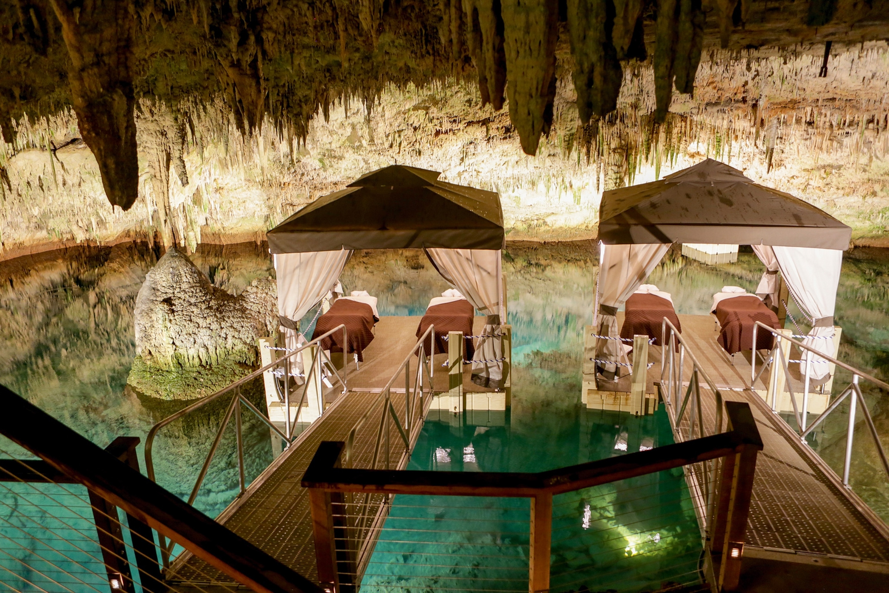 The interiors of a limestone cave with small bungalows floating on the still lake water.