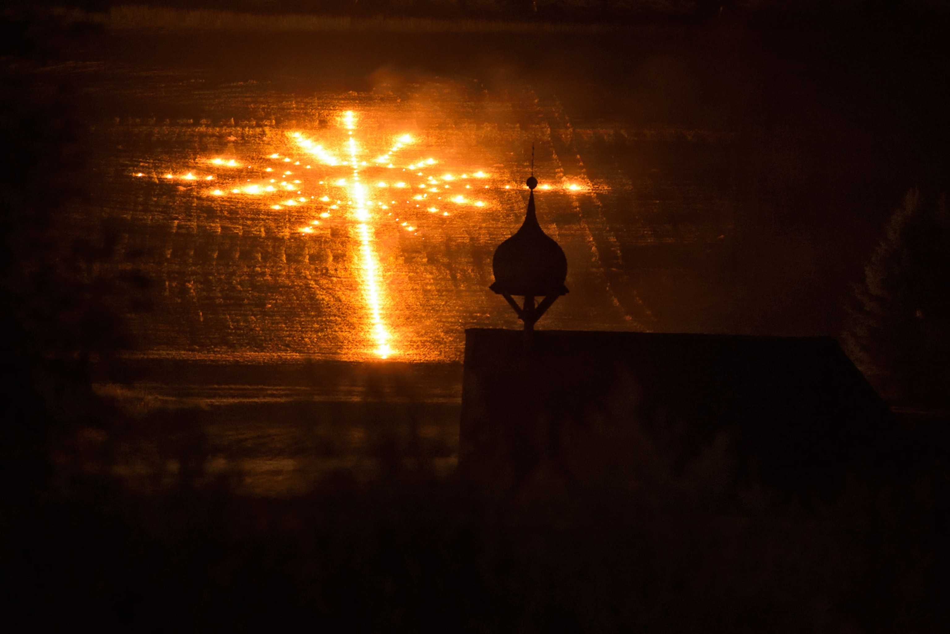 a sacred cross lit up with fire on the side of a moutain