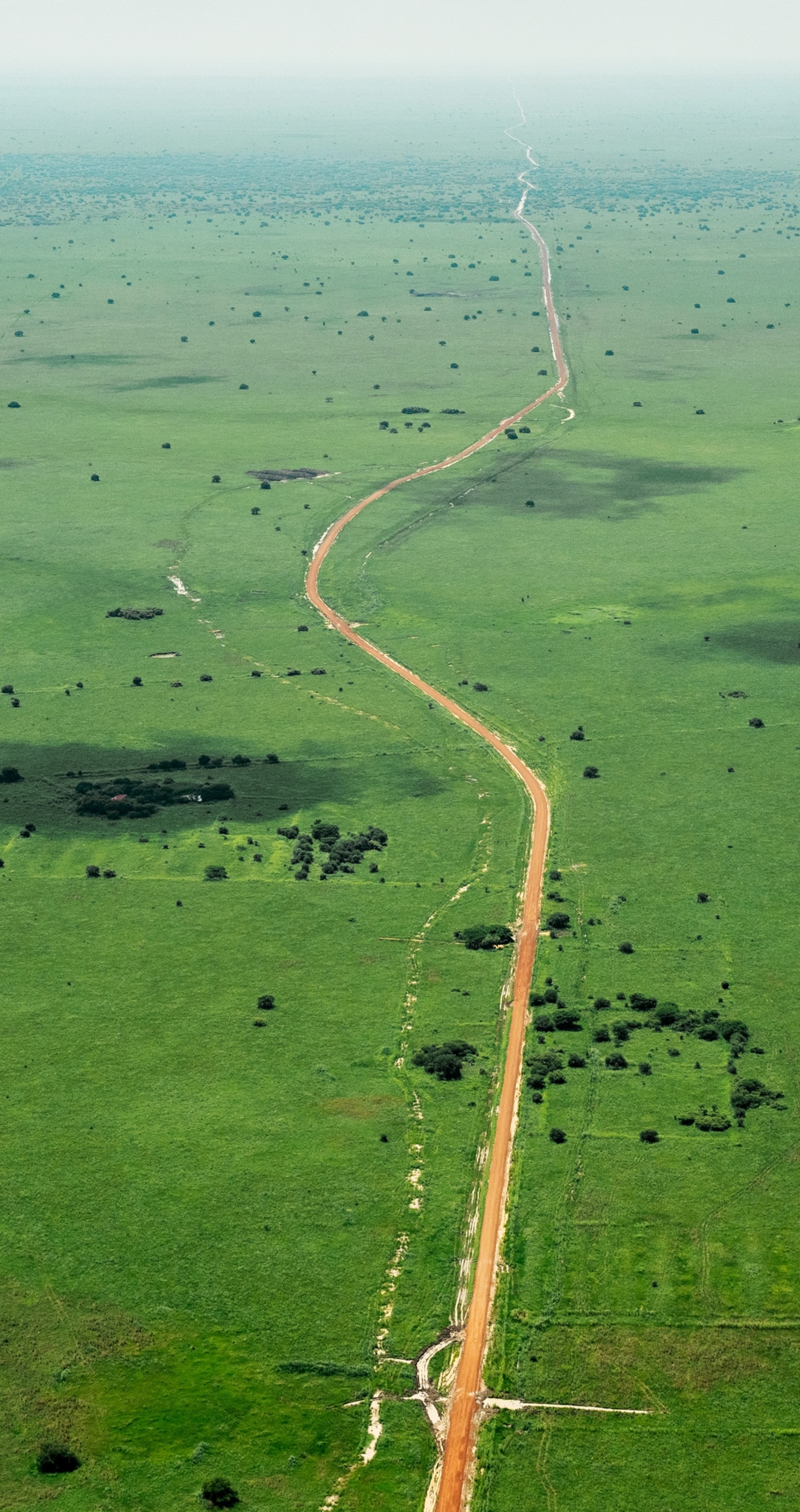 A long road stretches into the far distance over grassy terrain.